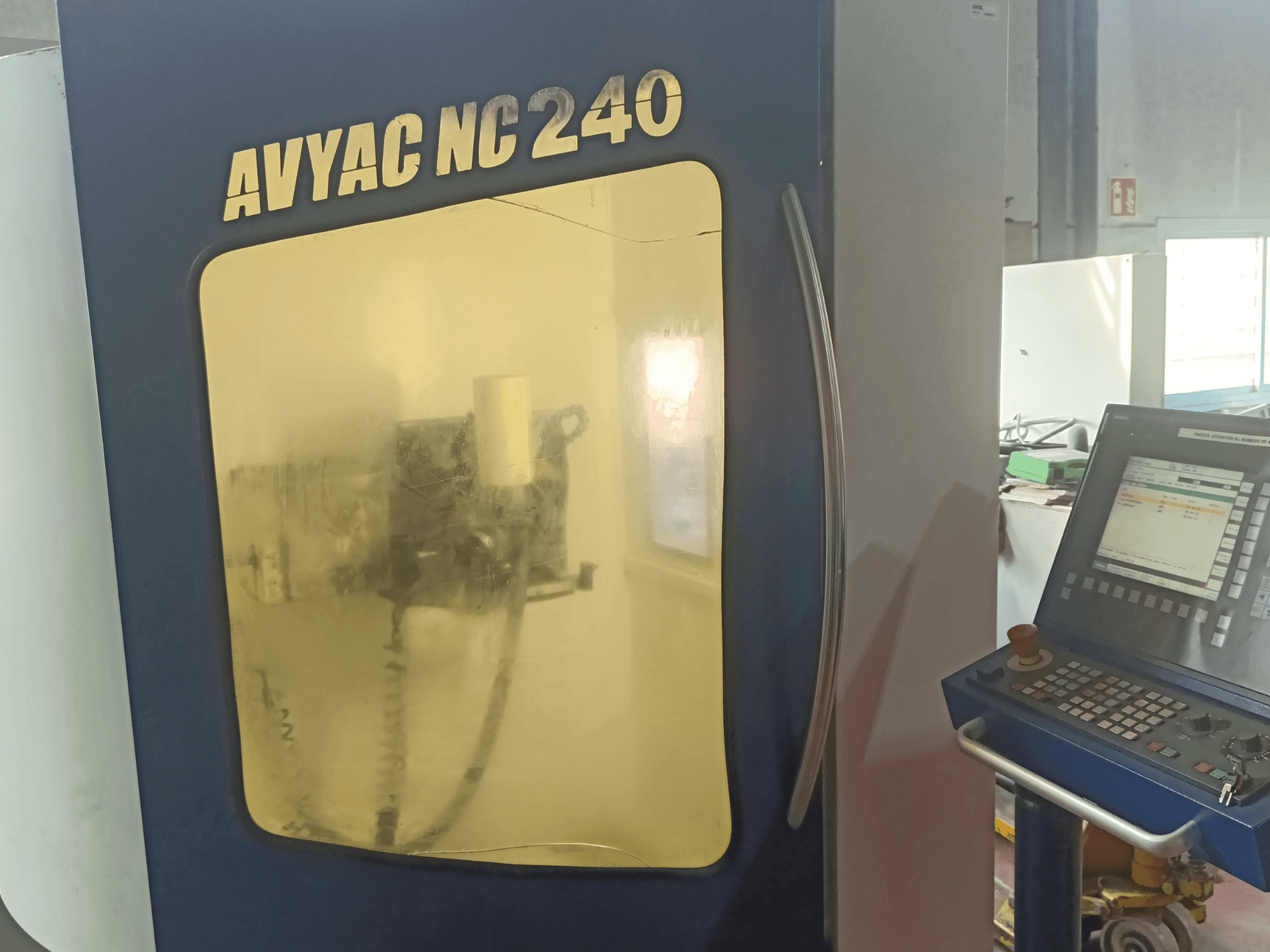 Rectifieuse cylindrique AVYAC NC240, vue latérale montrant le panneau de commande et la zone de rectification partiellement visible à travers la fenêtre.