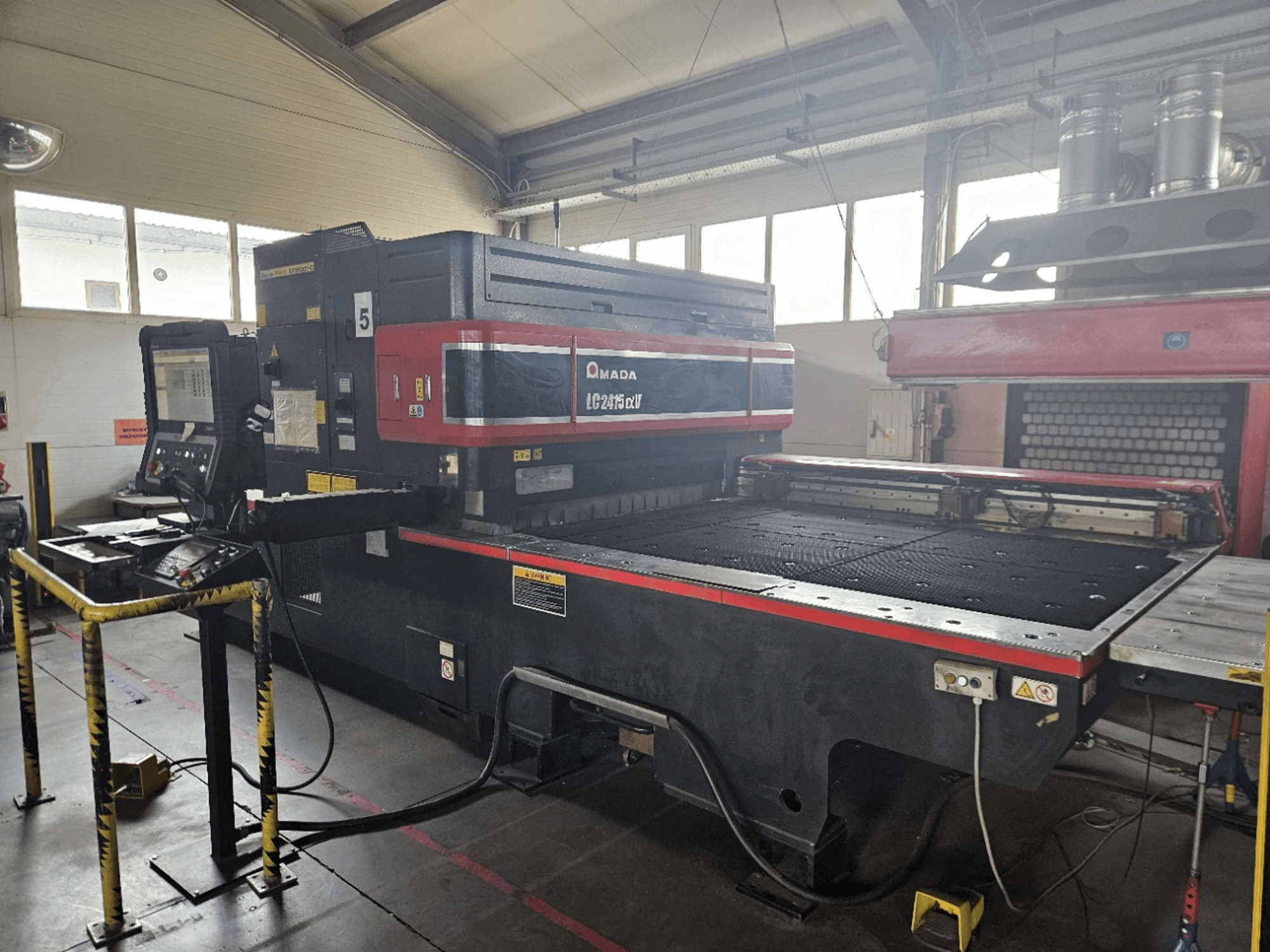 Machine de découpe laser CO₂ AMADA LC2415 Alpha 5, vue de face montrant le panneau de commande et le plateau de découpe avec ses barrières de sécurité.