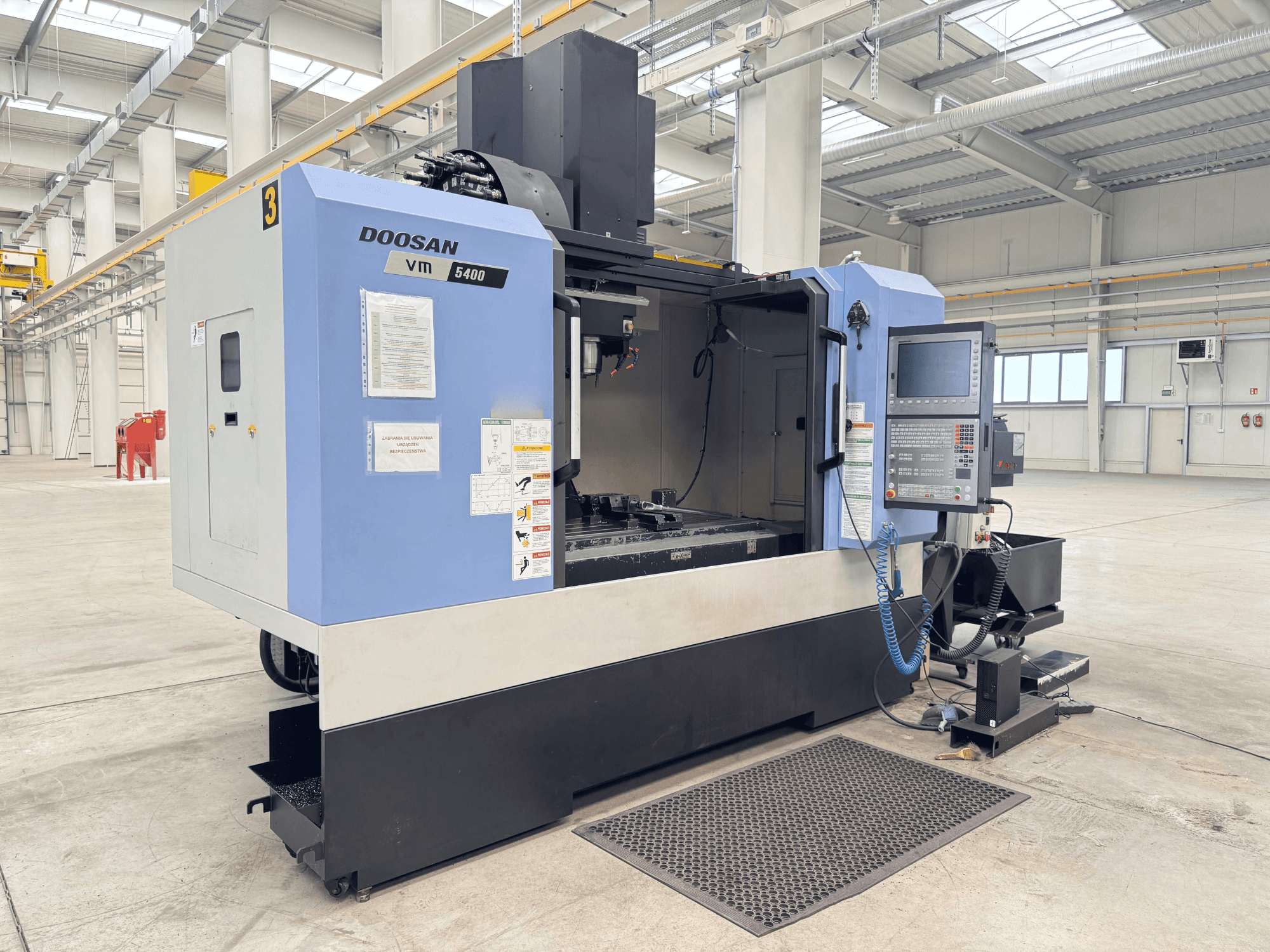 Centre d'usinage vertical DOOSAN VM 5400, vue de face montrant le panneau de commande et la zone de travail dans un environnement industriel spacieux.