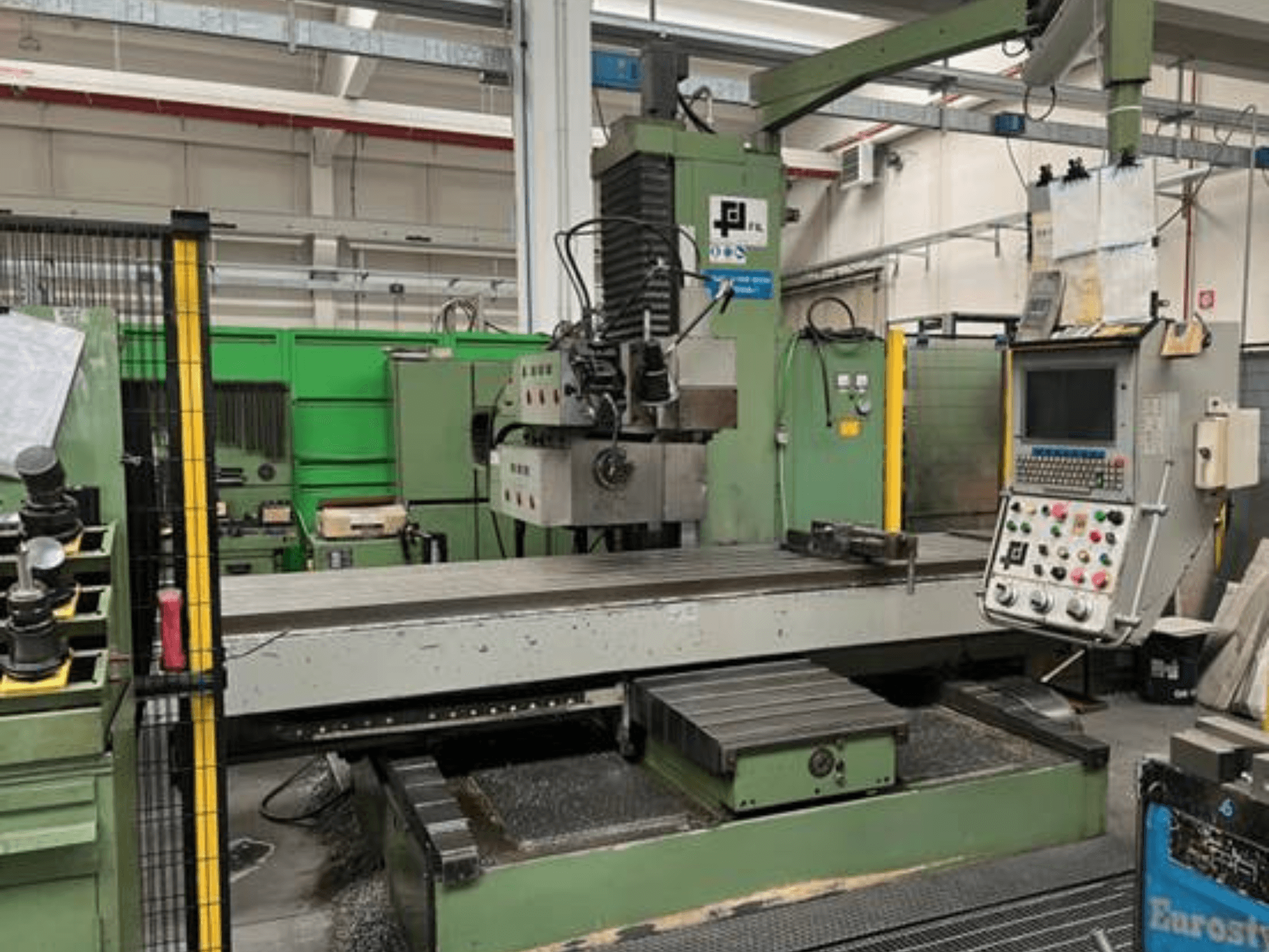 Fraiseuse industrielle de JFL, vue de face avec panneau de commande, grande table plate et copeaux de métal sur le sol.