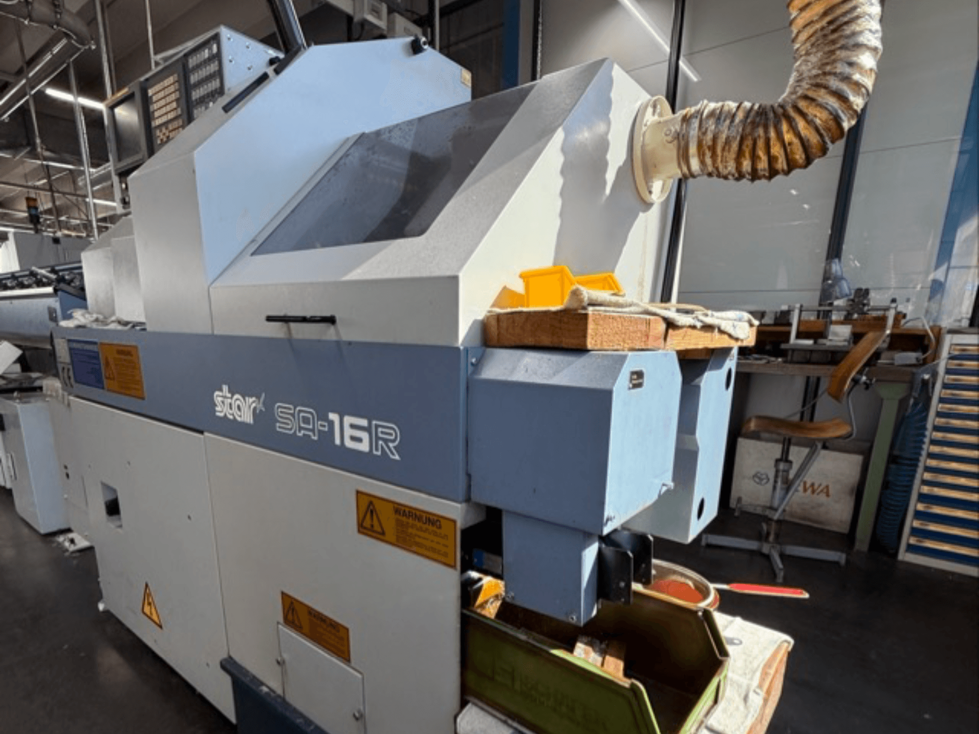 Machine Stark SA-16R vue de face, avec un échappement conique et un espace de travail avec des outils jaunes et des étiquettes d'avertissement.