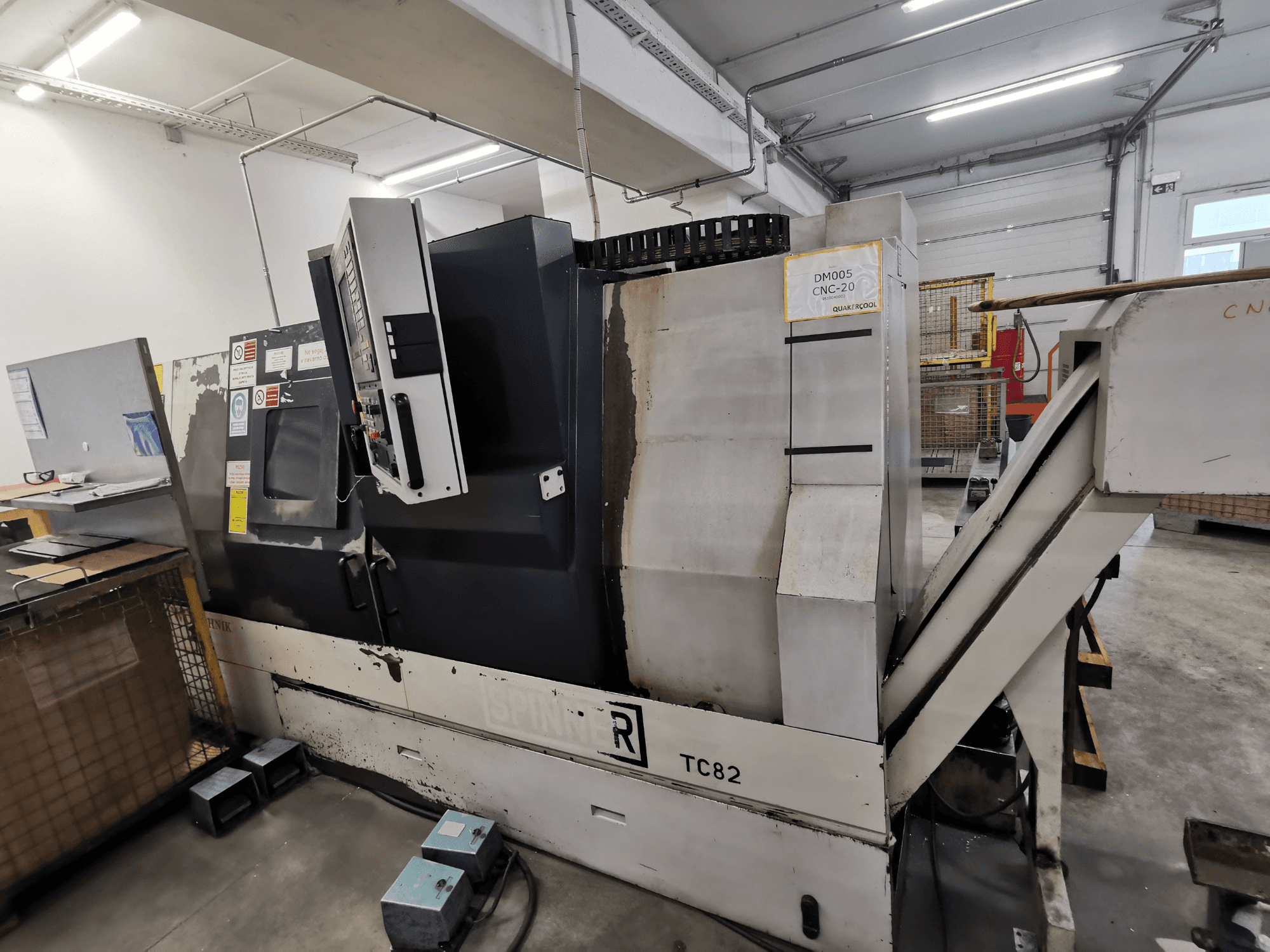 Machine CNC, marque Spinner, modèle TC82, vue latérale montrant le panneau de commande et la goulotte d'évacuation des déchets dans un atelier.