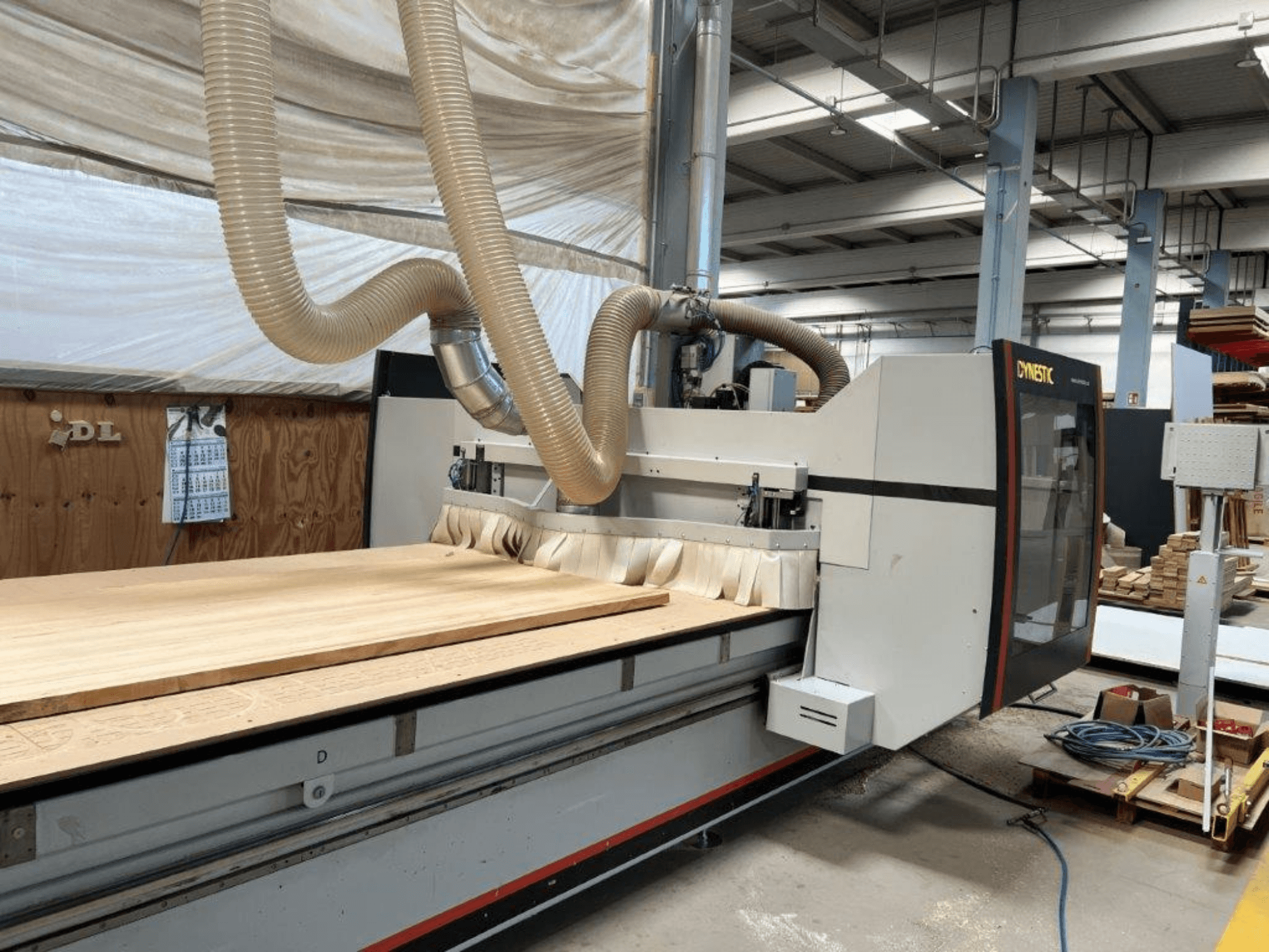 Machine CNC de Dynestic, vue de face, avec une grande pièce en bois et un tuyau d'extraction de la poussière dans un atelier.