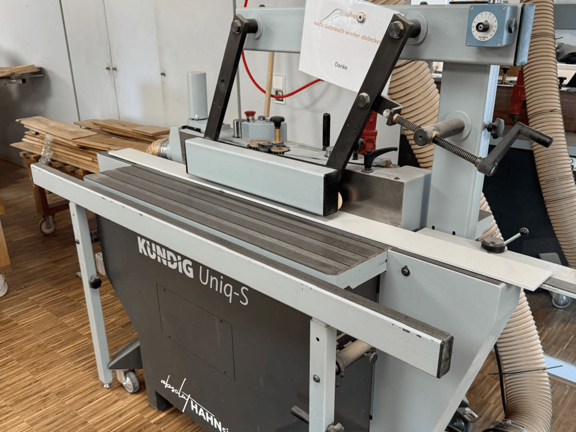 Ponceuse à bande Kundig UNIQ-S dans un atelier, vue latérale montrant la bande abrasive et les bras de support réglables.