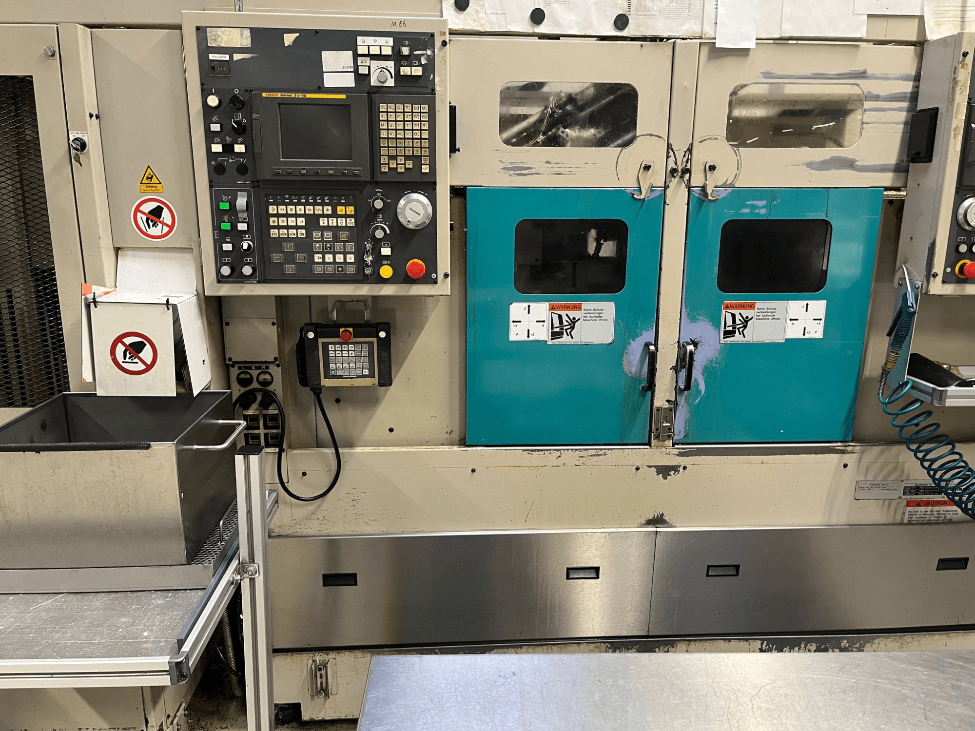 Panneau de commande d'une machine de fabrication avec des portes de couleur sarcelle, des avertissements de sécurité et un clavier ; vue de face, finition en acier inoxydable.