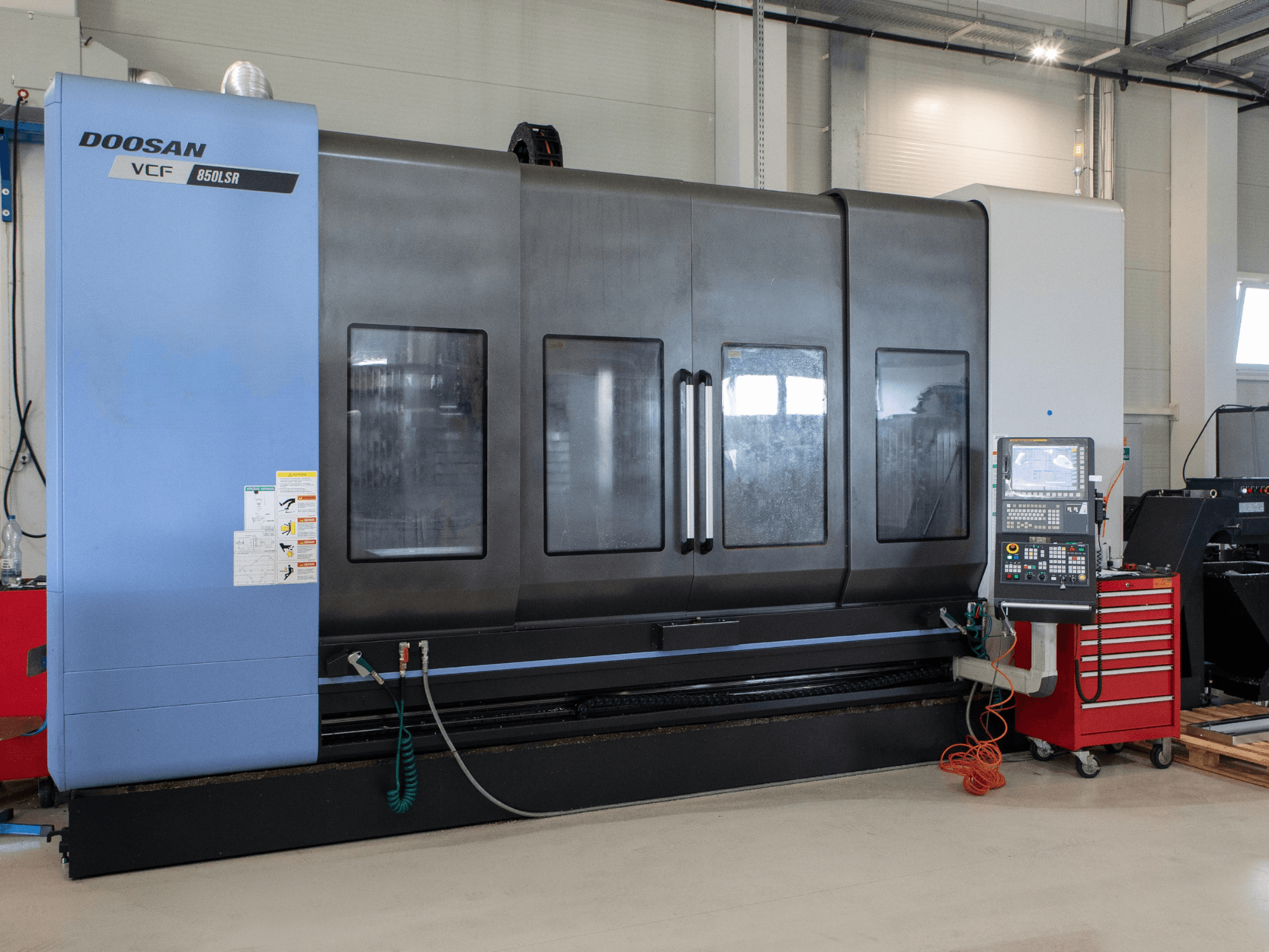 Centre de fraisage-tournage DOOSAN VCF850, vue de face ; il est équipé de deux grandes fenêtres, d’un panneau de commande et d’un compartiment de rangement pour les outils. Idéal pour l’usinage.