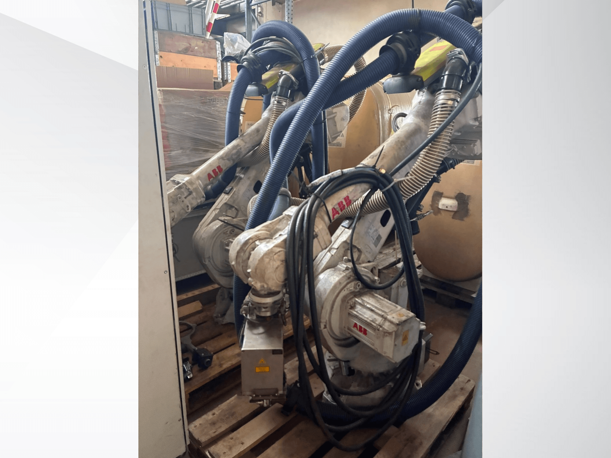 Bras robotisé ABB IRB 4600-40/2,55, vue de profil montrant les deux bras et les flexibles raccordés, monté sur des palettes dans un entrepôt.
