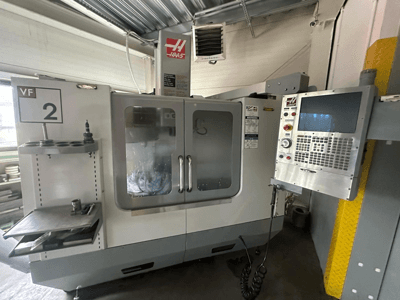 Machine CNC Haas VF-2, vue de face, comprenant les commandes, le porte-outil et les portes transparentes avec l'outillage visible à l'intérieur de l'armoire.
