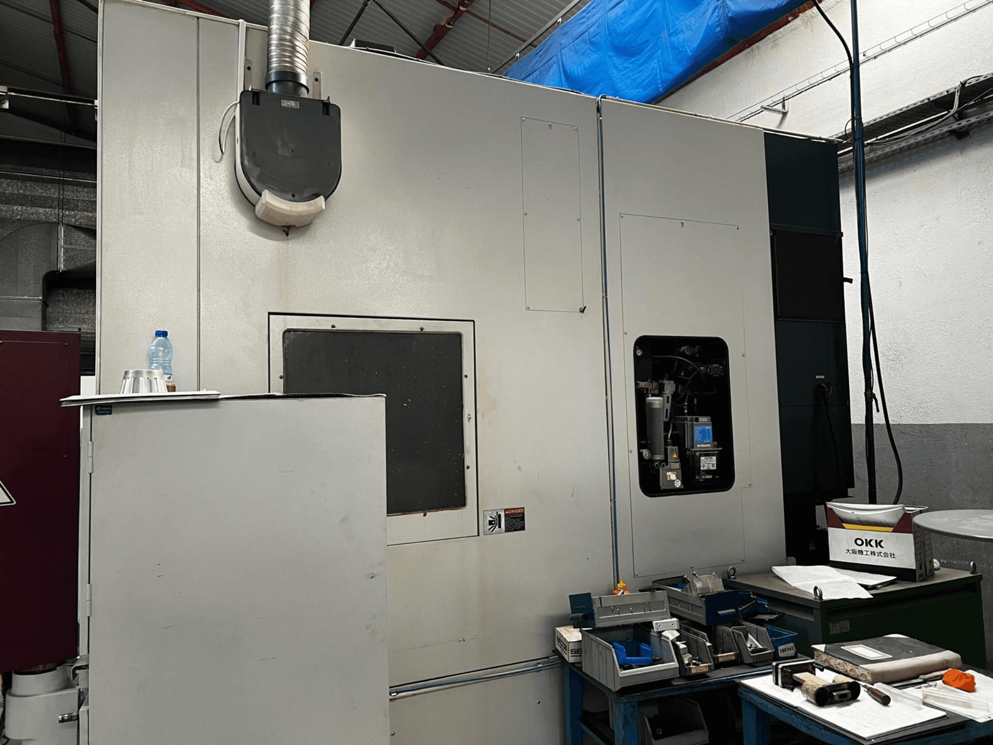 Centre d'usinage vertical OKK VP600 dans un atelier, vue de profil montrant les détails de la machine et les outils posés sur une table à proximité.