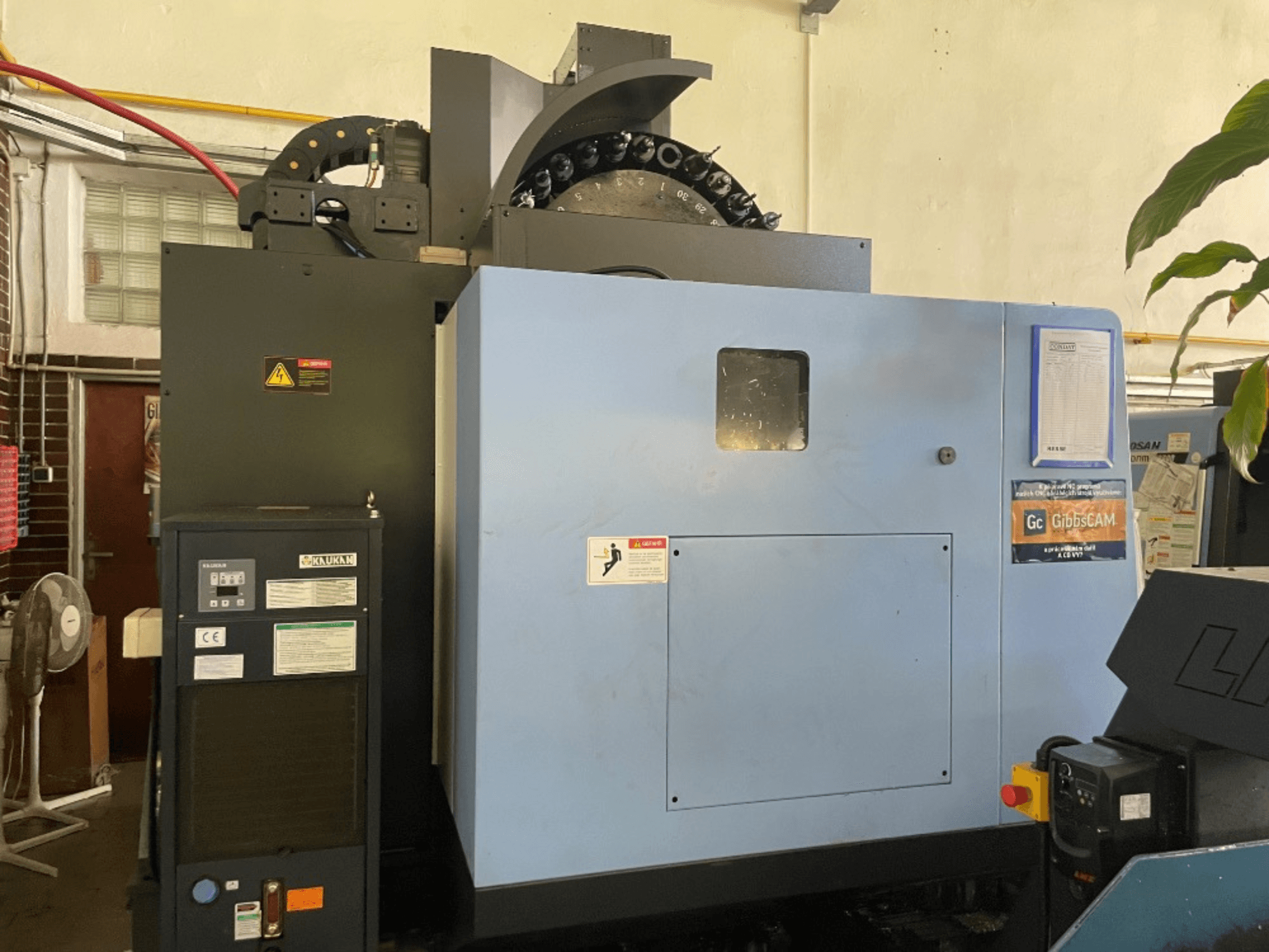 Vue avant d'un centre d'usinage vertical DOOSAN DNM 5700, montrant le panneau de commande, les étiquettes de sécurité et les caractéristiques de la machine.