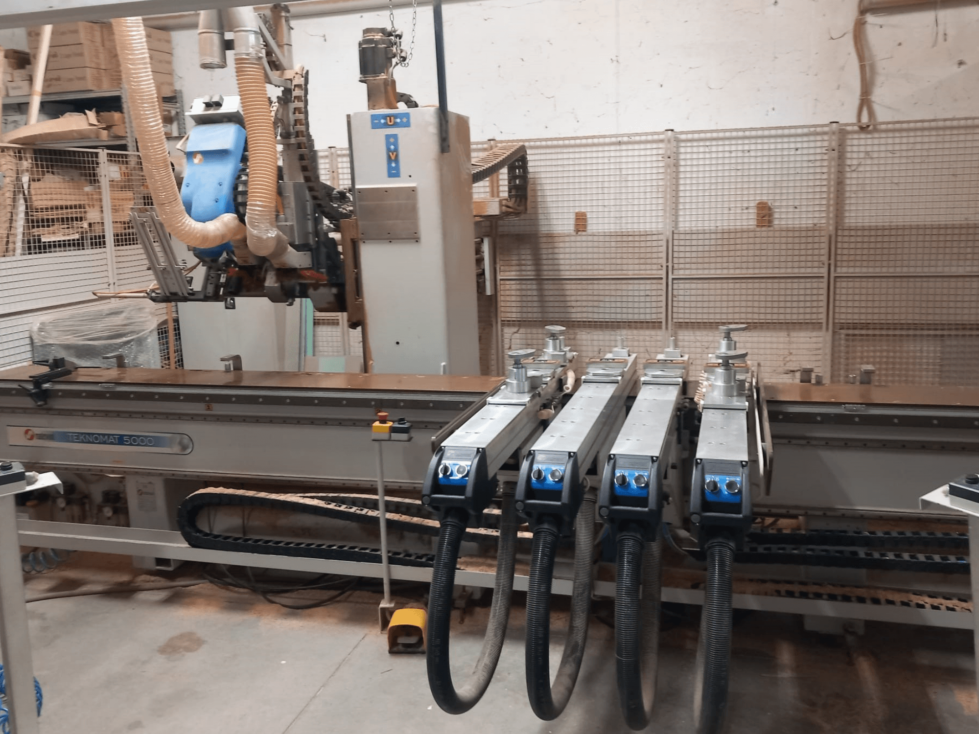 Centre d'usinage CNC du bois MASTERWOOD TEKNOMAT 5000, vue de face mettant en évidence la tête d'usinage et les différents tuyaux d'aspiration.