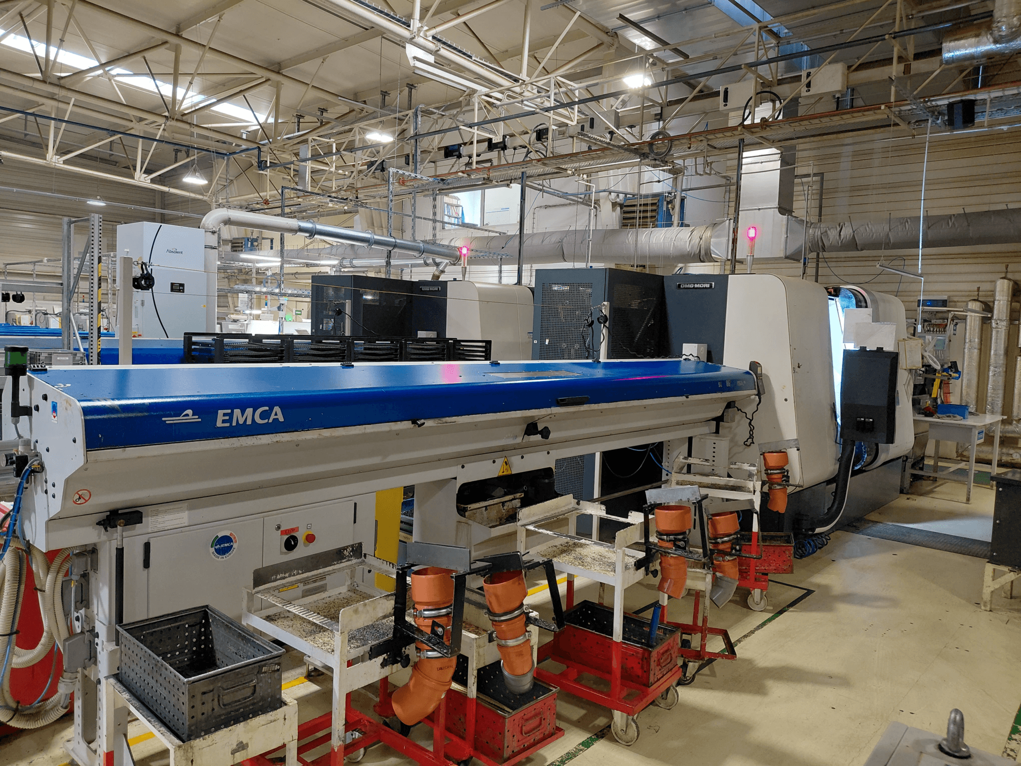 Tour multibroche linéaire DMG MORI Sprint 65 dans un atelier, vue latérale montrant l'automatisation EMCA et la configuration de l'outillage.