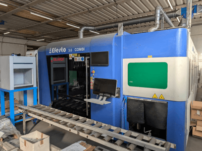 Machine de découpe au laser à fibre EFESTO 3.6 COMBI, vue de profil, avec panneau de commande et voyants de sécurité, dans un boîtier bleu.