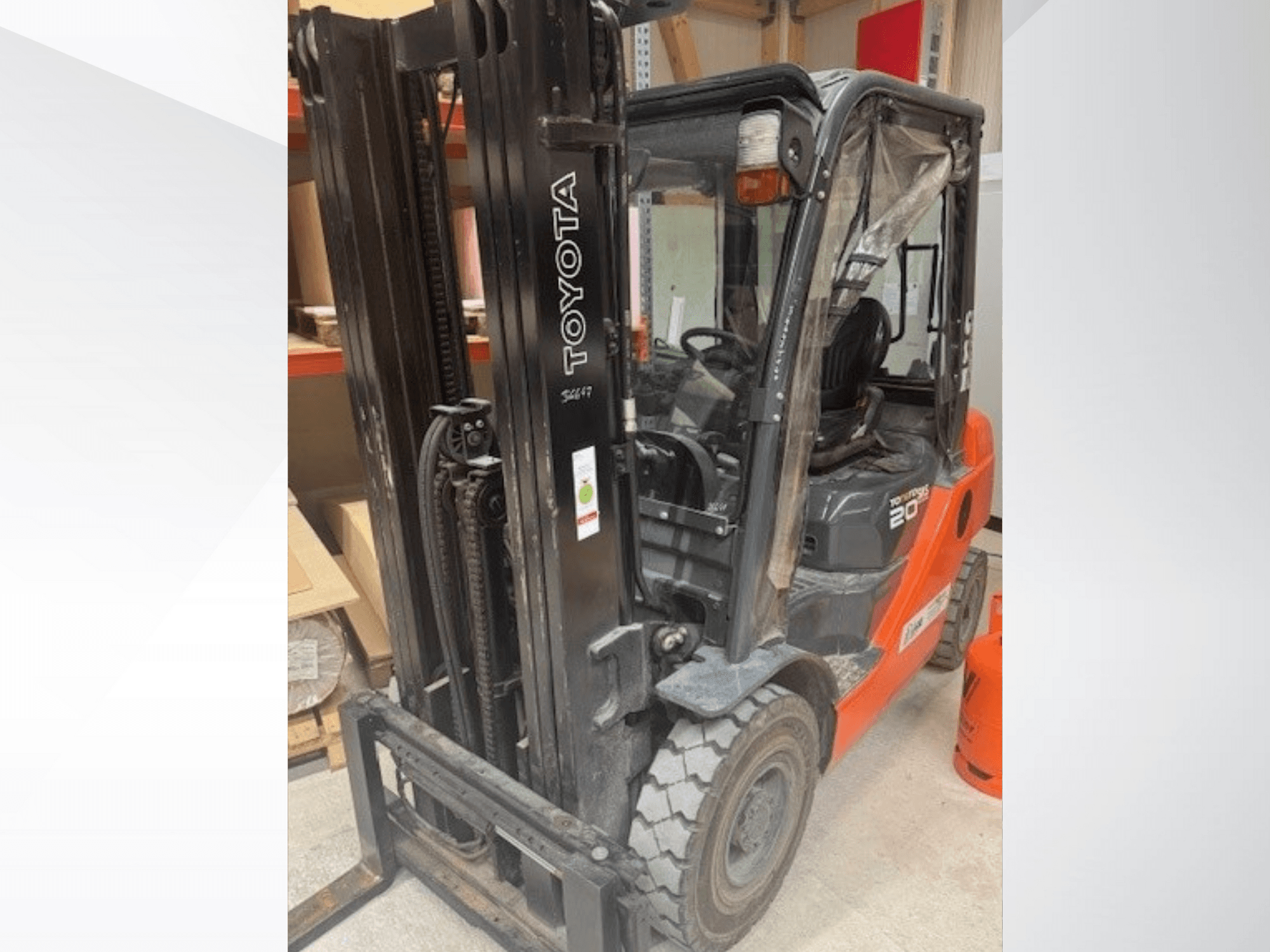 Chariot élévateur Toyota 20 vu de face, avec un mât noir, une cabine transparente et une bouteille de propane orange à côté.
