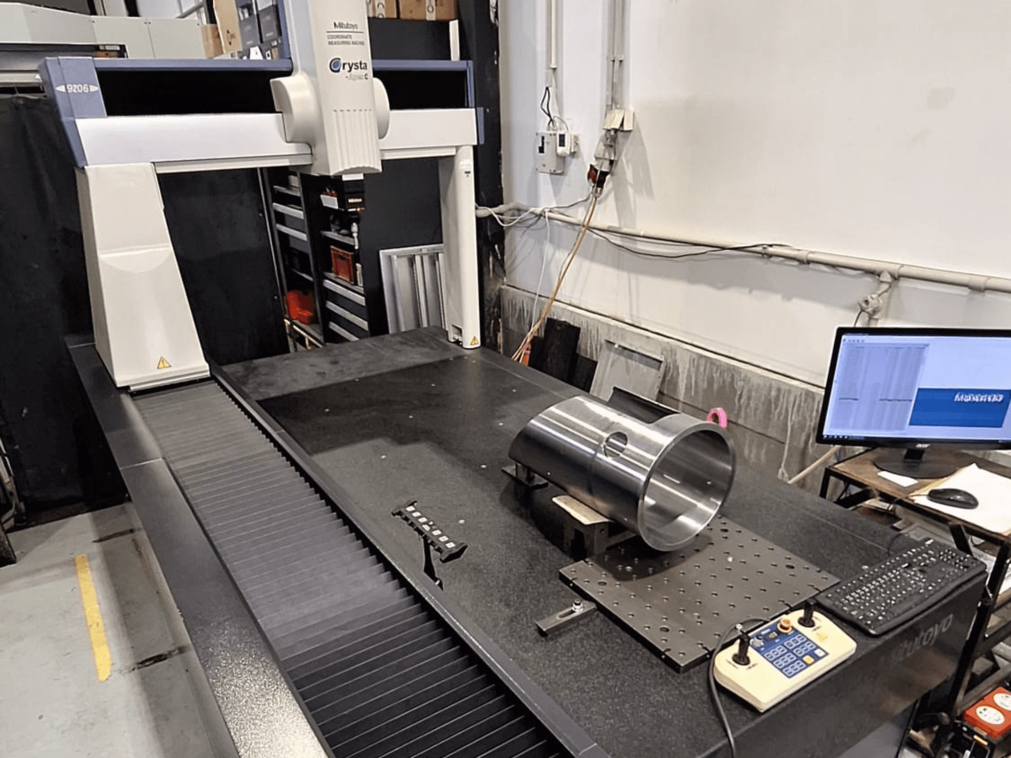 MMT Mitutoyo Crysta-Apex C9206 en vue de face, mesurant une pièce métallique cylindrique sur une plaque de surface en granit noir.