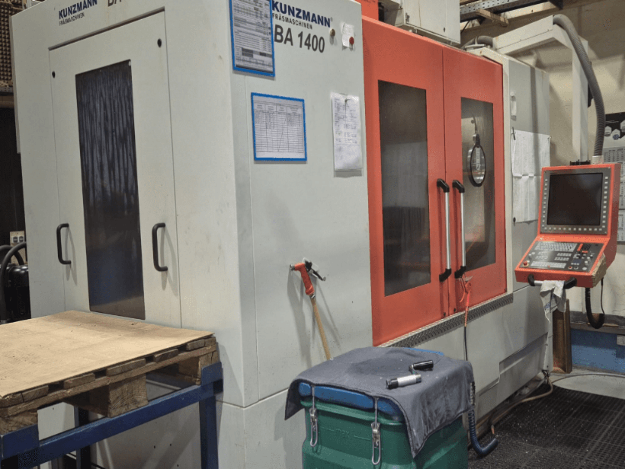 Vue avant du centre d'usinage vertical KUNZMANN BA1400, avec les portes orange, le panneau de commande et la table de travail.