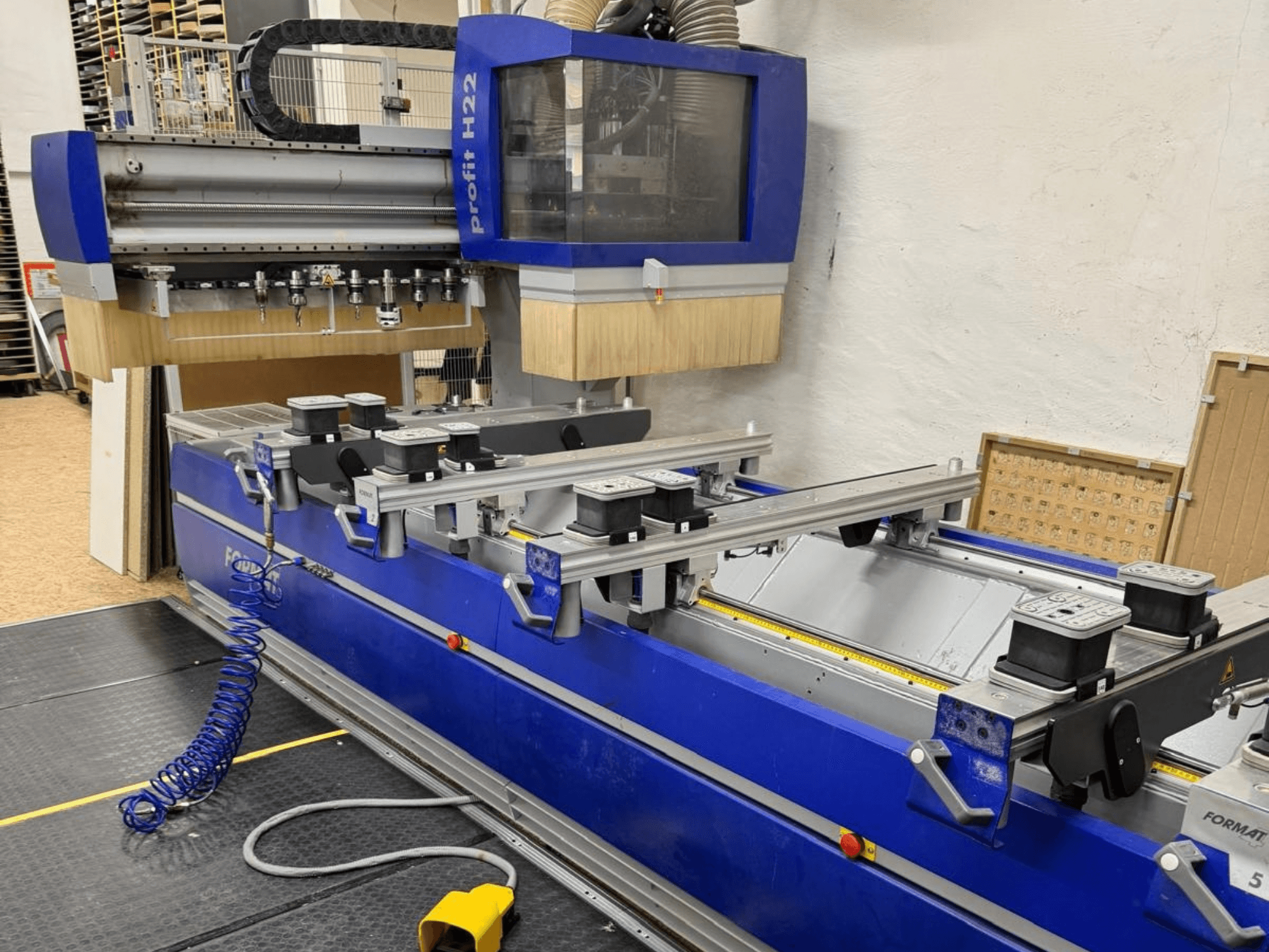 Centre d'usinage du bois CNC FORMAT4 PROFIT H22, vue de face, avec les outils d'usinage et les pinces de serrage visibles sur le châssis bleu.