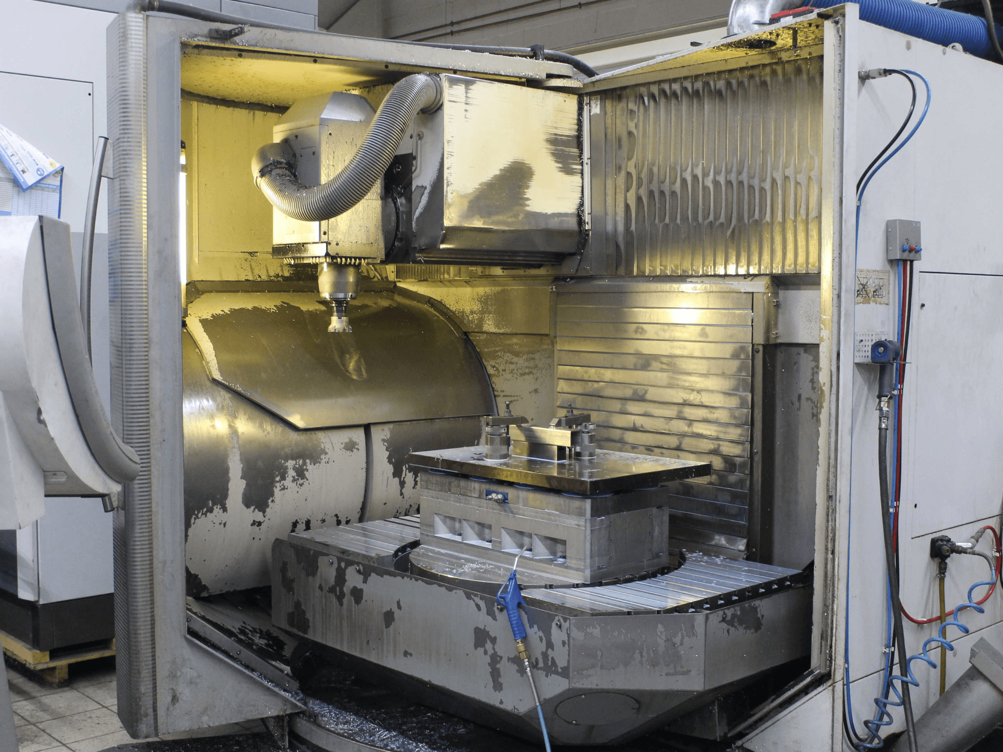 Intérieur d'une fraiseuse CNC, vue latérale, montrant la pièce à usiner et l'outil de coupe avec des copeaux de métal et des résidus de liquide de refroidissement.