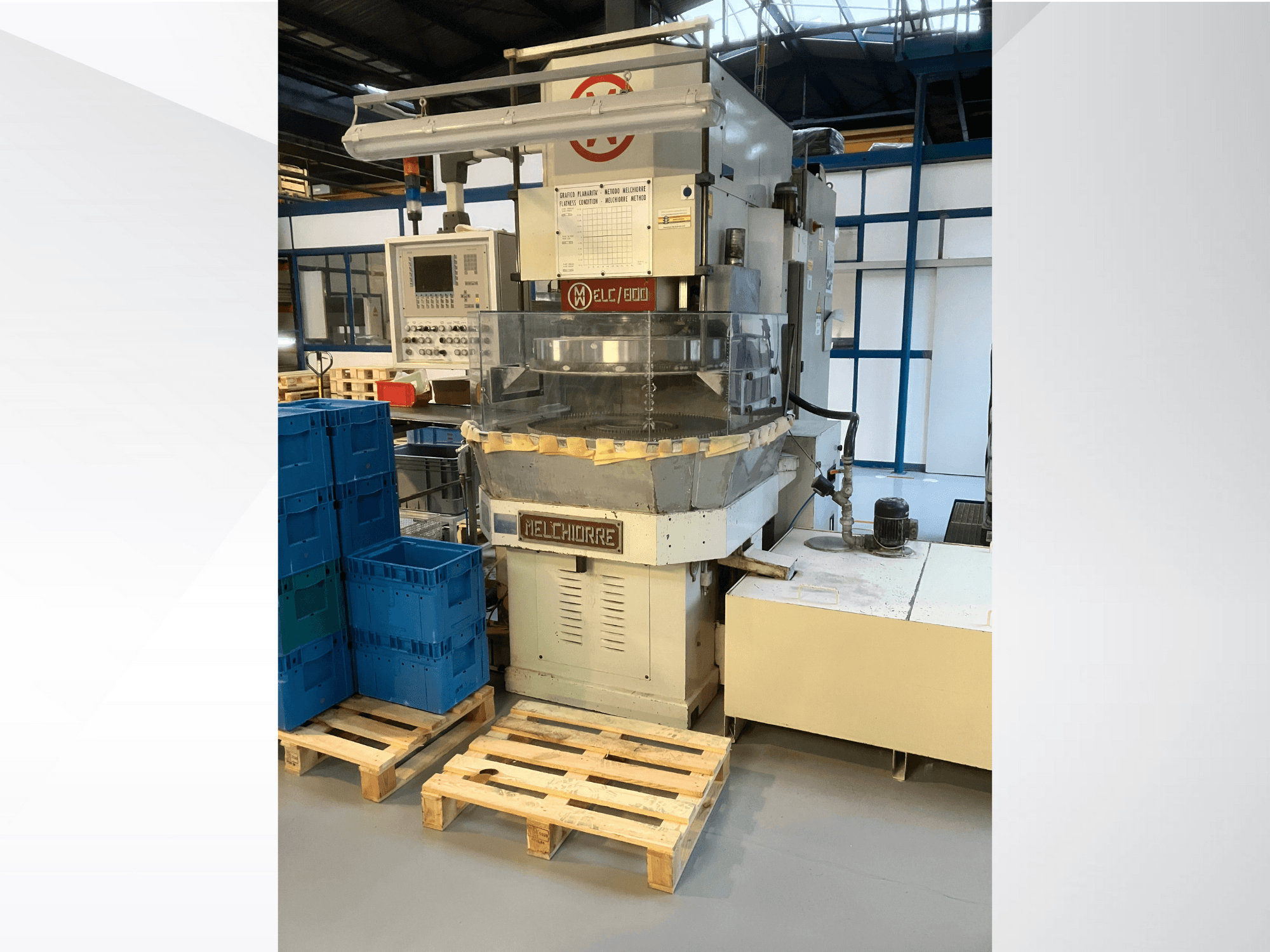 Machine industrielle Melchiorre vue de face, avec panneau de commande, trémie transparente et caisses bleues sur palettes en bois.
