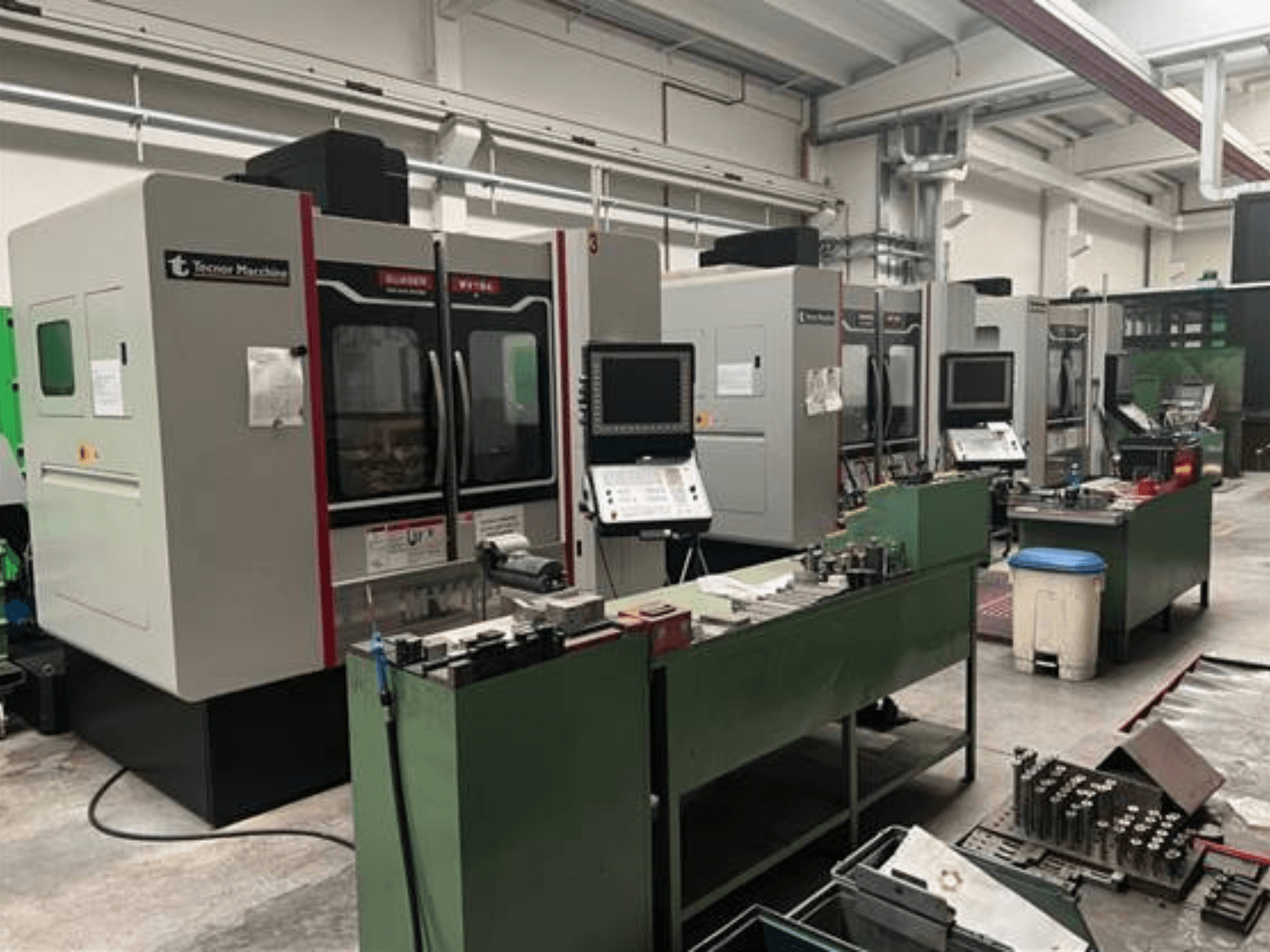 Quatre machines CNC de Tecnoer Marchine dans un atelier, vue de face, avec des outils et des pièces sur des établis verts.