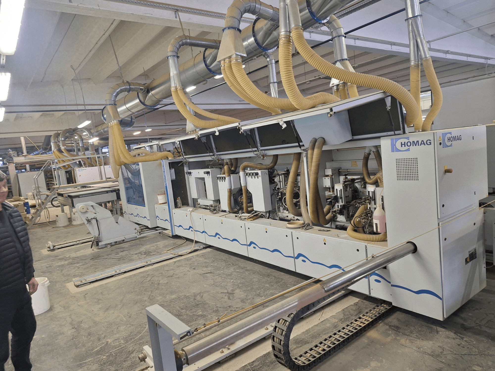 Machine à bois HOMAG dans une usine, vue de face montrant les multiples broches et le système d'extraction de la poussière.