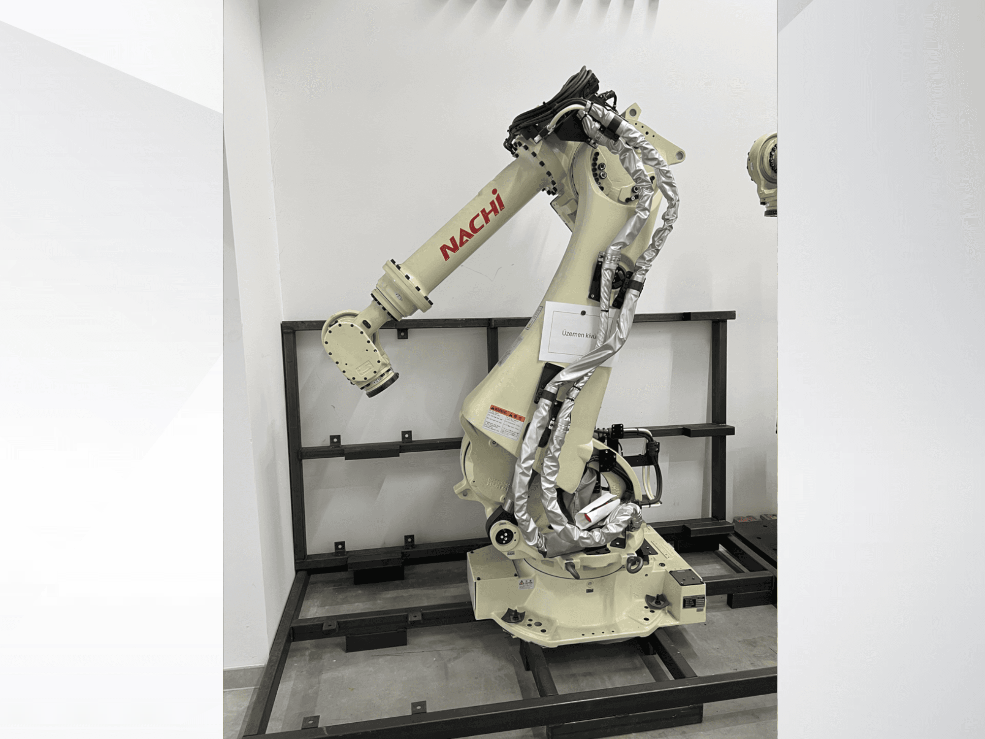 Bras robotique NACHI SRA166-01 en vue latérale, doté d'articulations flexibles, de câbles attachés et monté sur un cadre de protection.
