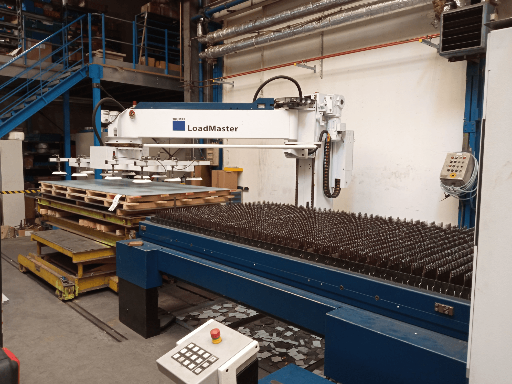 Machine de découpe laser CO₂ TRUMPF TruLaser 3030 vue de profil, équipée d'un LoadMaster et de palettes de matériaux.