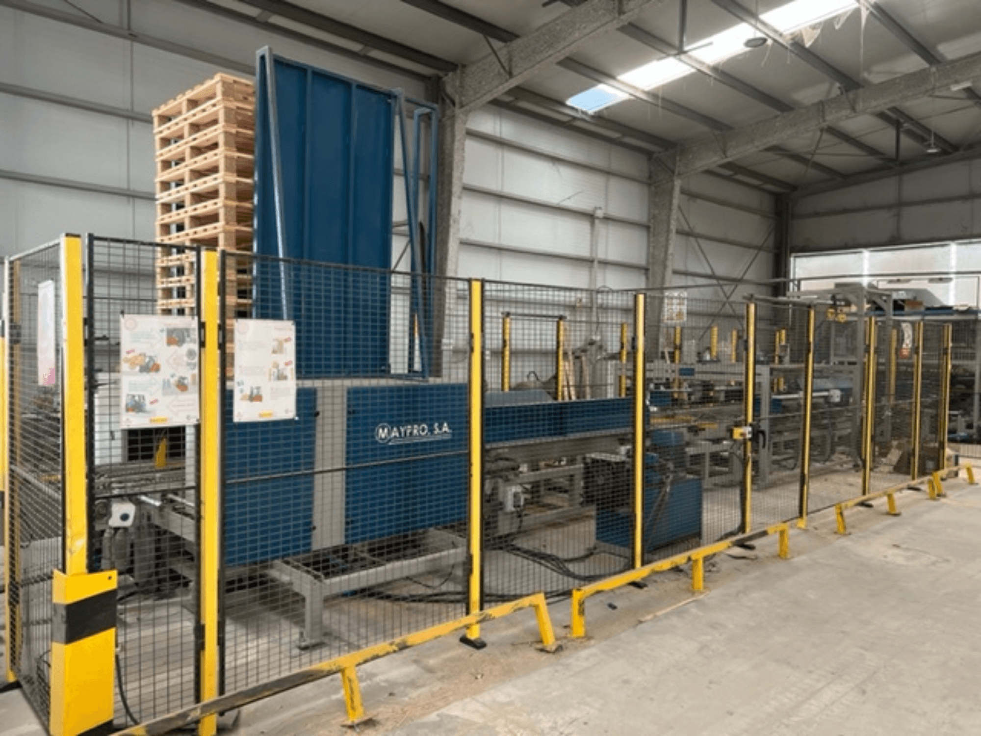 Machine industrielle d'emballage de palettes de Maypro S.A. dans un entrepôt, avec filet de sécurité et commandes opérationnelles, vue de côté.