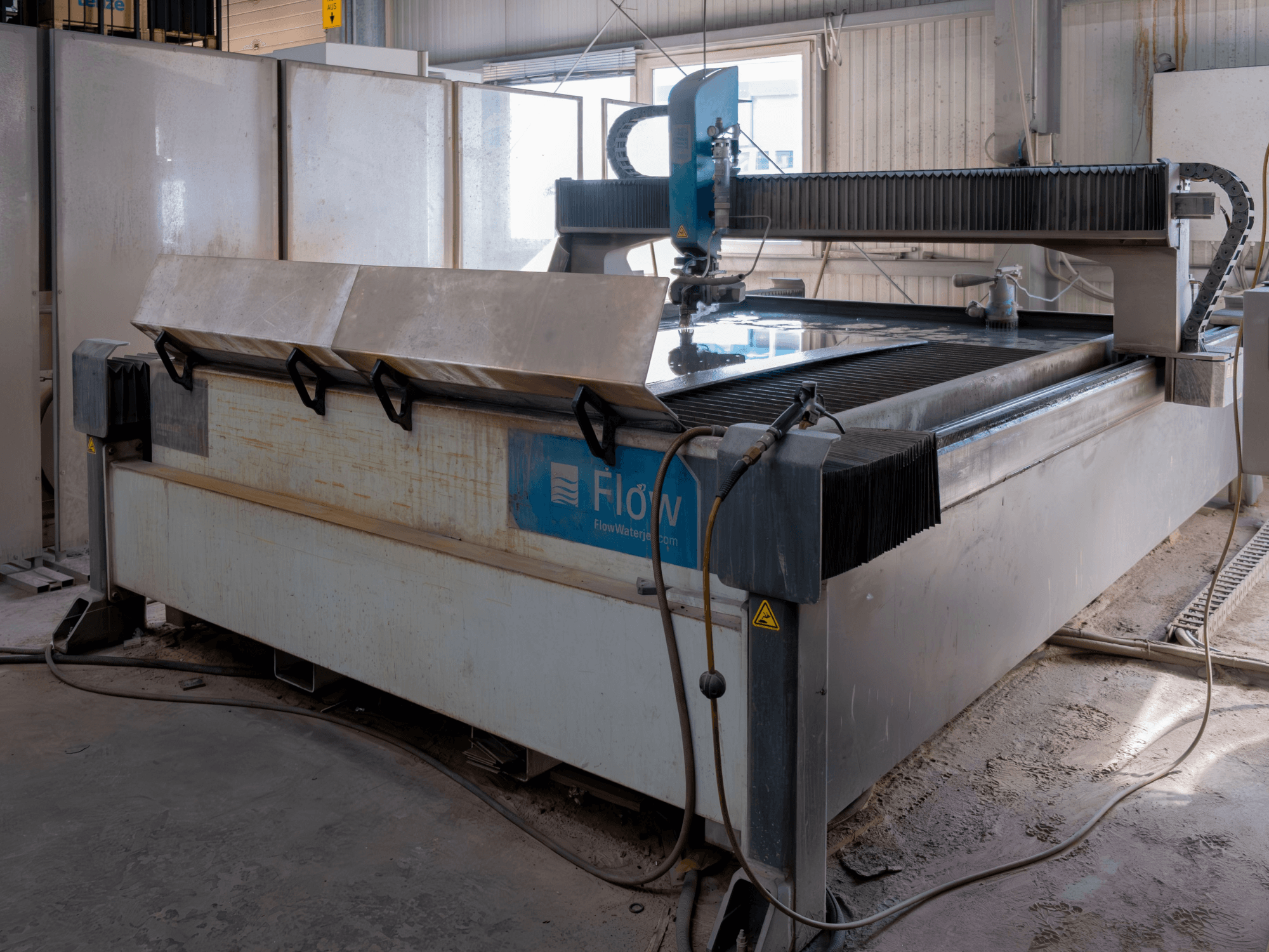 Machine de découpe au jet d'eau Flow KENT Mach 2 C vue de côté, présentant la table de découpe en acier inoxydable et la buse de jet d'eau.