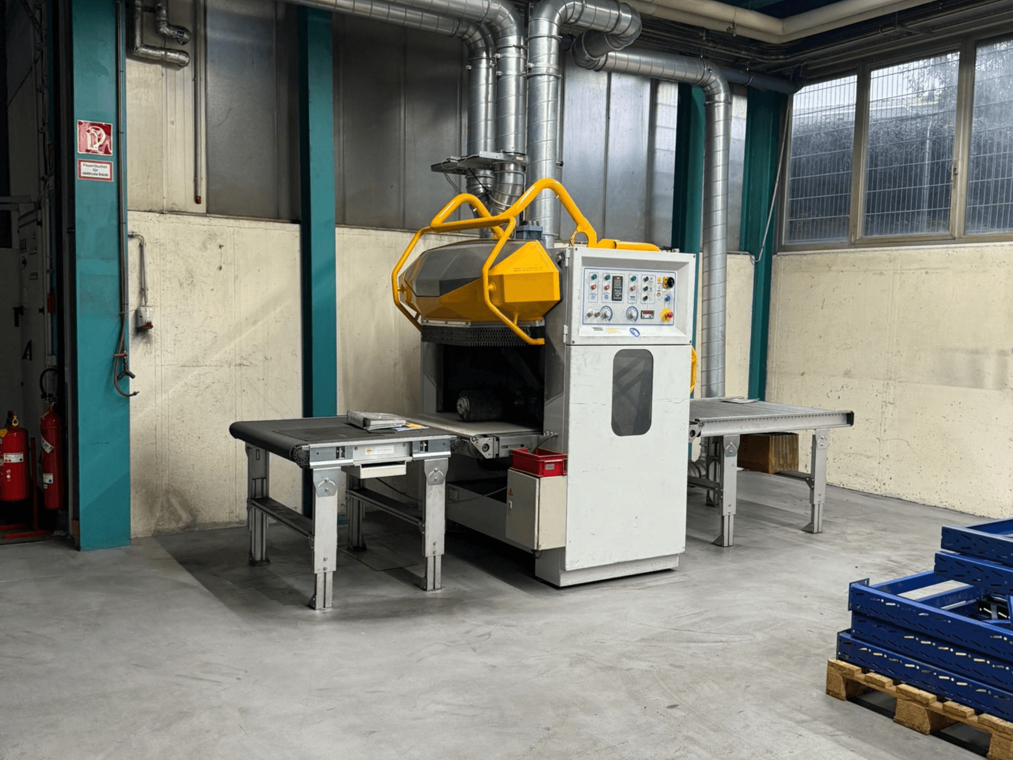Machine à ébavurer Fladder AUT-1000 VAC dans une usine, avec un panneau de commande, une protection jaune et des tables de travail adjacentes.