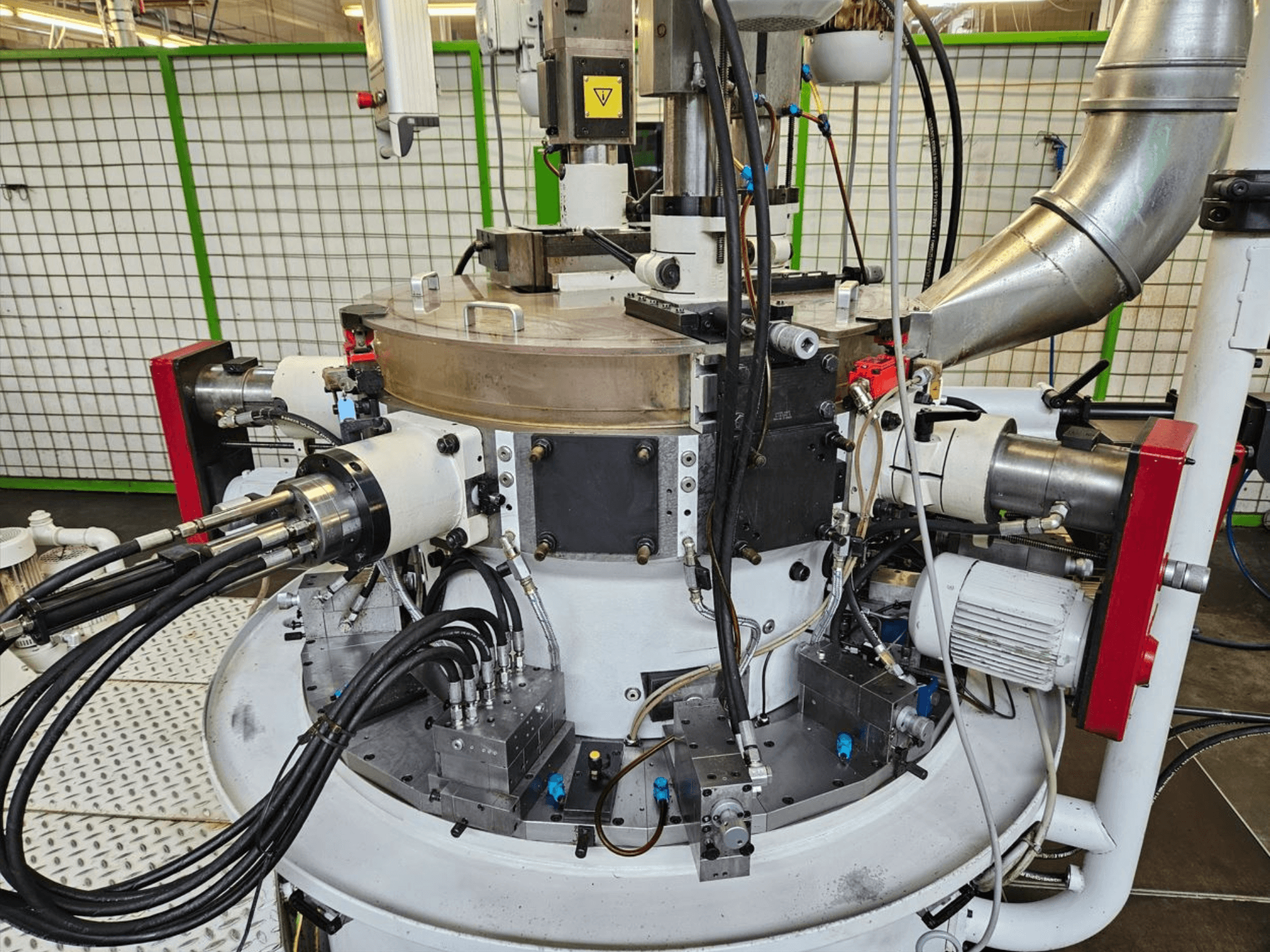 Vue rapprochée d'une machine industrielle avec des tuyaux hydrauliques, des composants métalliques et une base rotative. Aucune marque n'est visible.