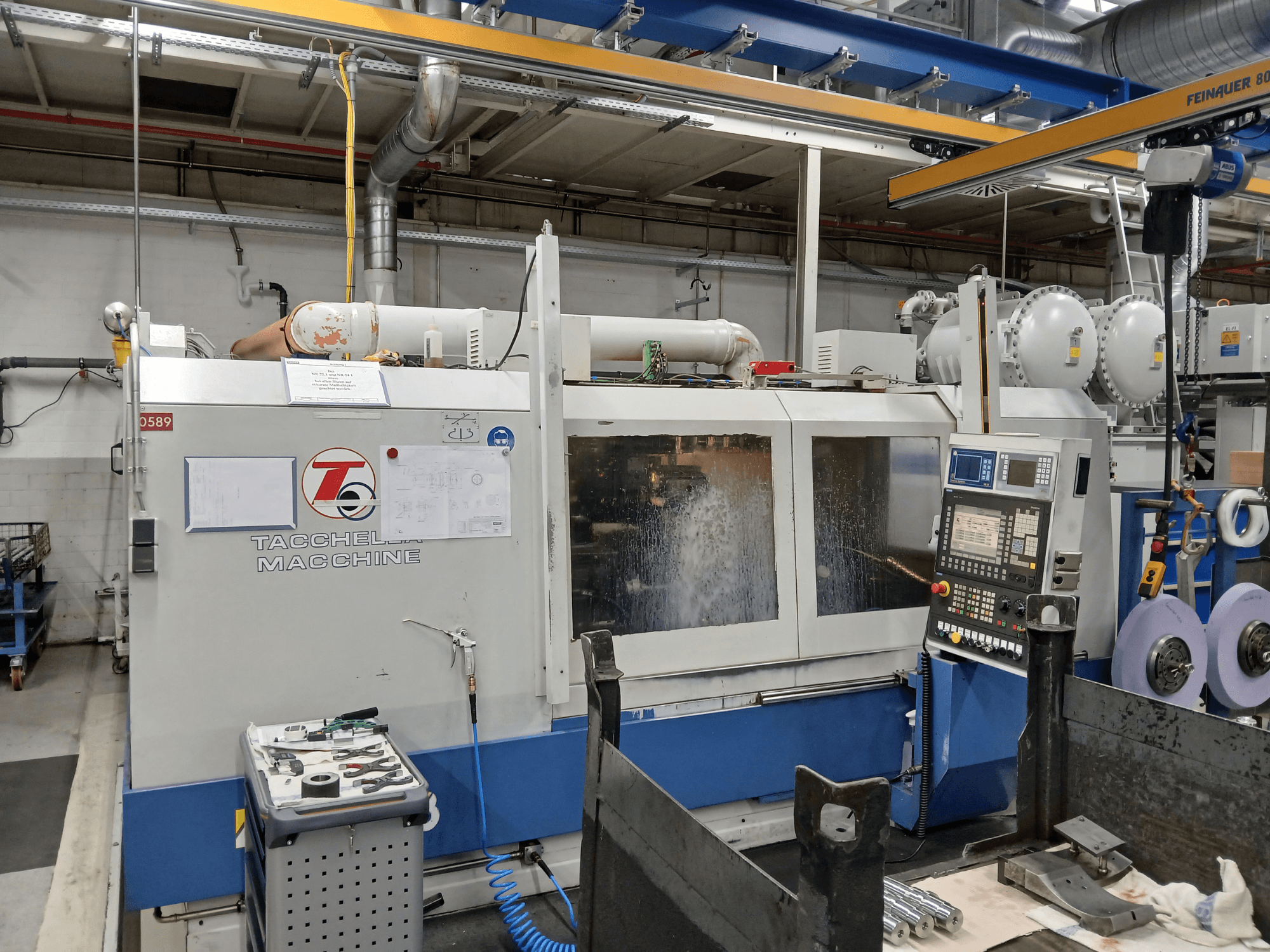 Centre d'usinage Tacchella vu de face, avec le panneau de commande et les outils visibles. L'eau de refroidissement est pulvérisée pendant le fonctionnement.