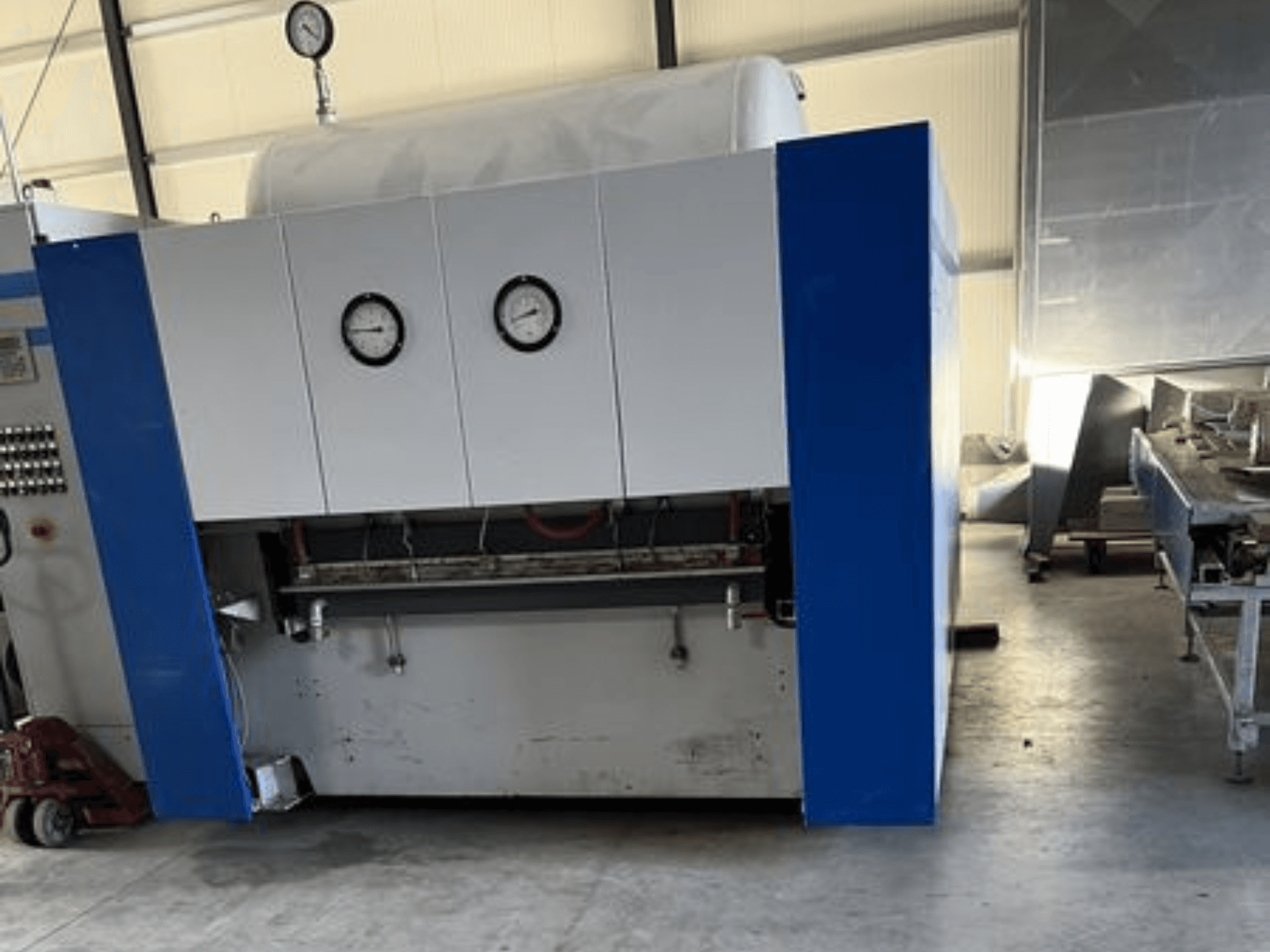 Machine industrielle bleue et blanche avec deux manomètres, vue de face, comportant un panneau de commande et des équipements adjacents.