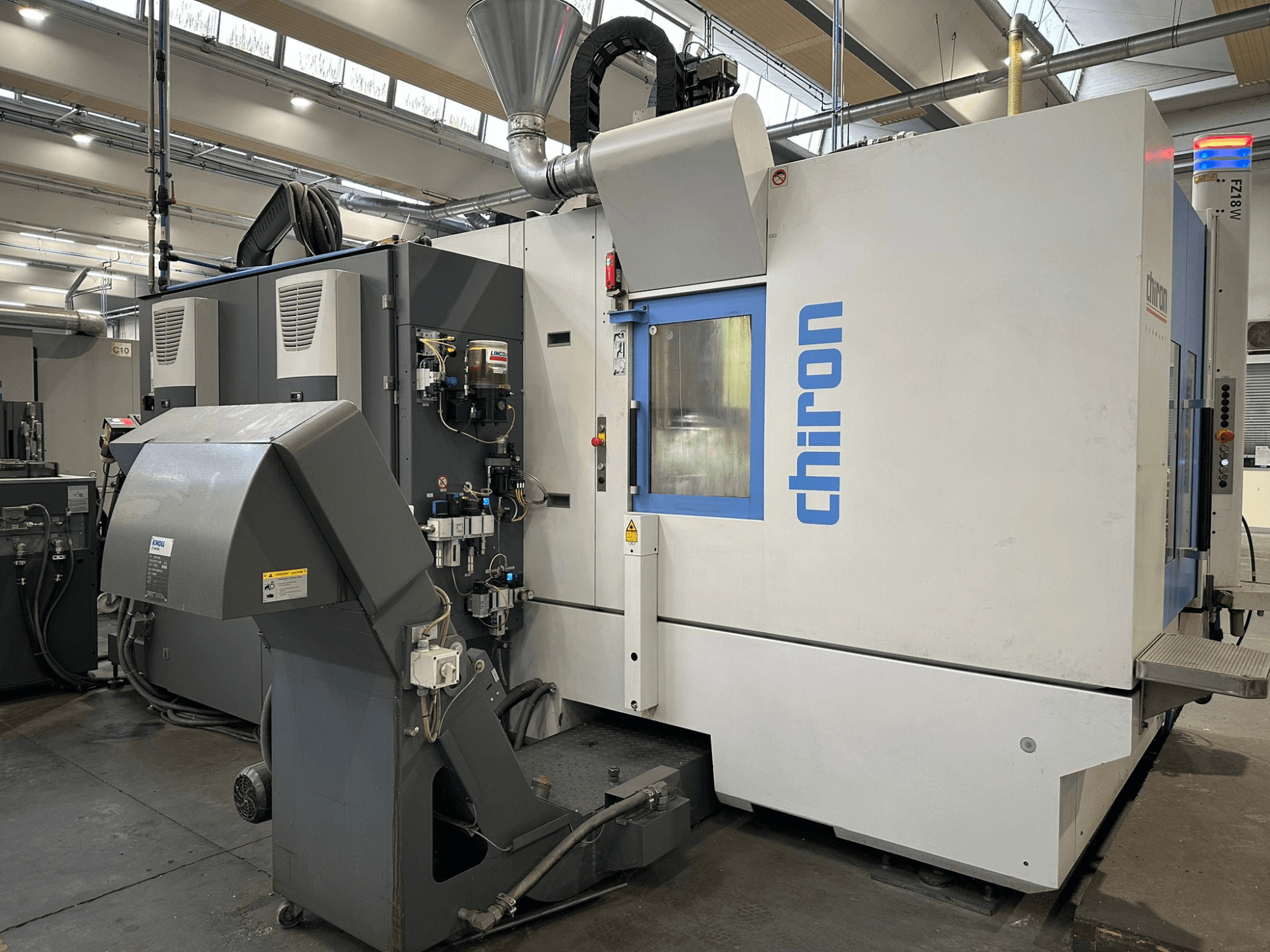 Machine CNC Chiron en gris et blanc, vue de face, avec commandes, tuyaux et capot d'extraction de la poussière.