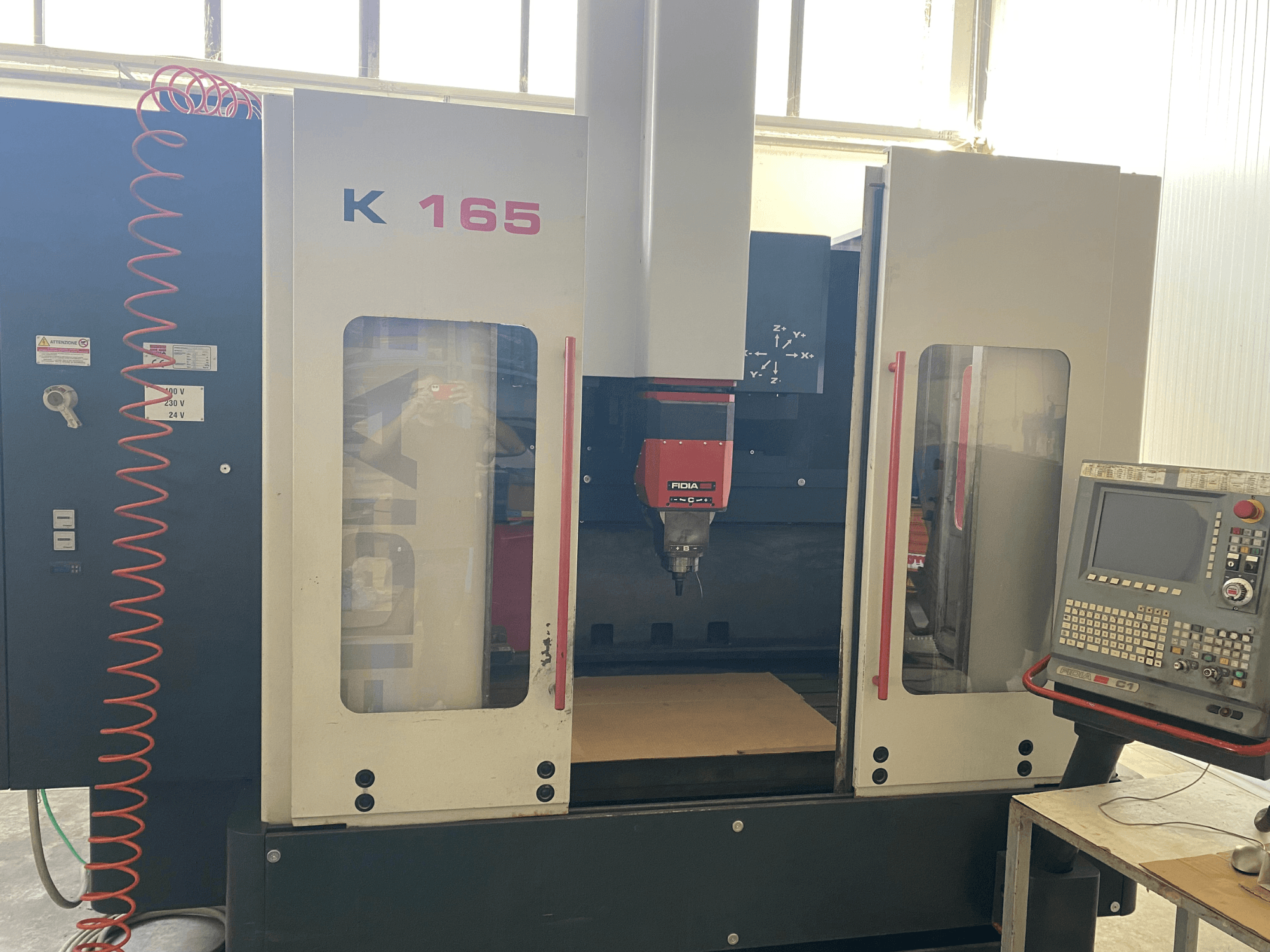 Machine CNC Fidia K 165 avec broche et panneau de commande rouges, vue de face, dans un atelier bien éclairé.