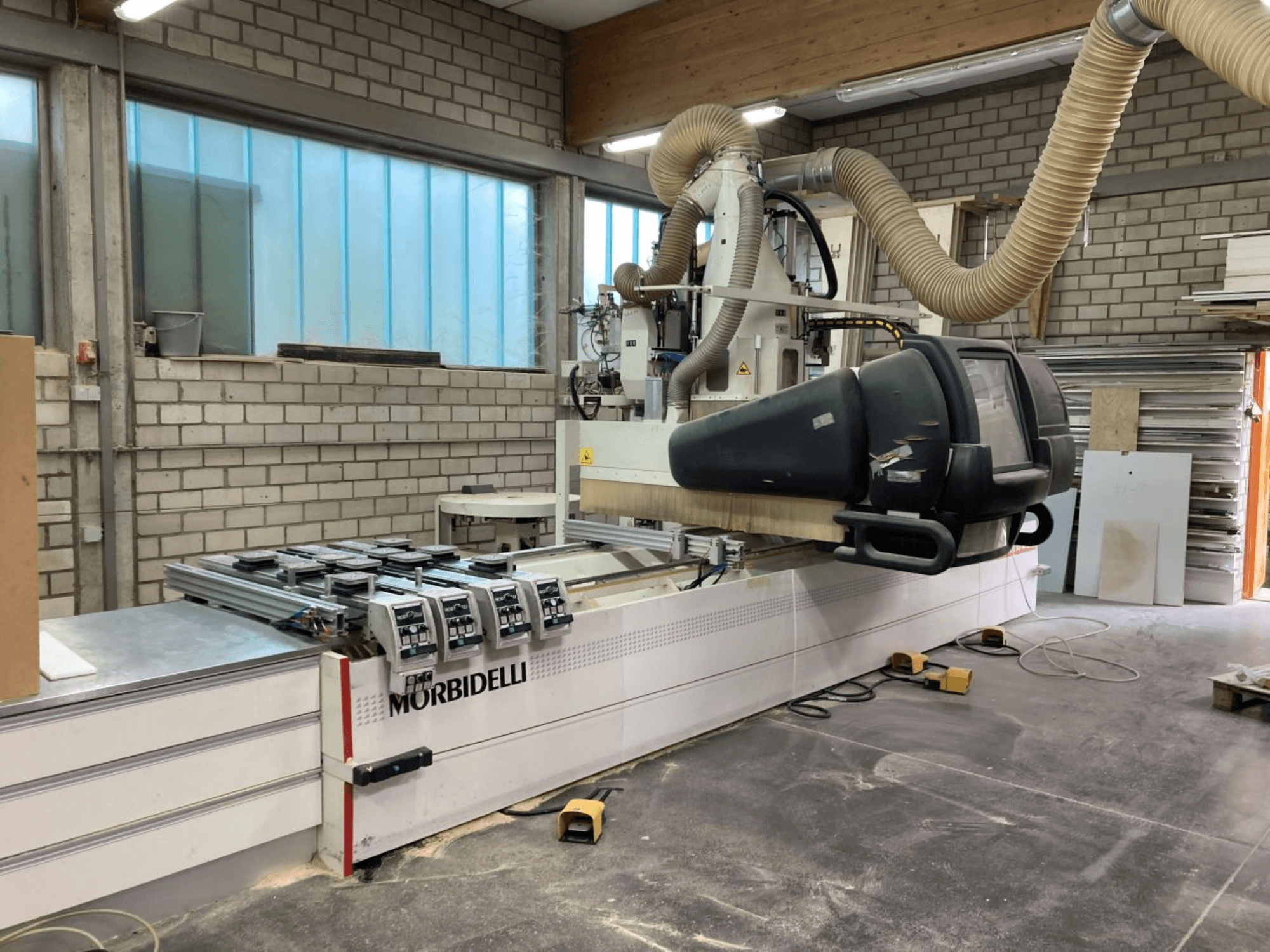Machine CNC MORBIDELLI dans un atelier, vue de face avec le panneau de commande, le système d'extraction des poussières et la pièce de bois positionnée.