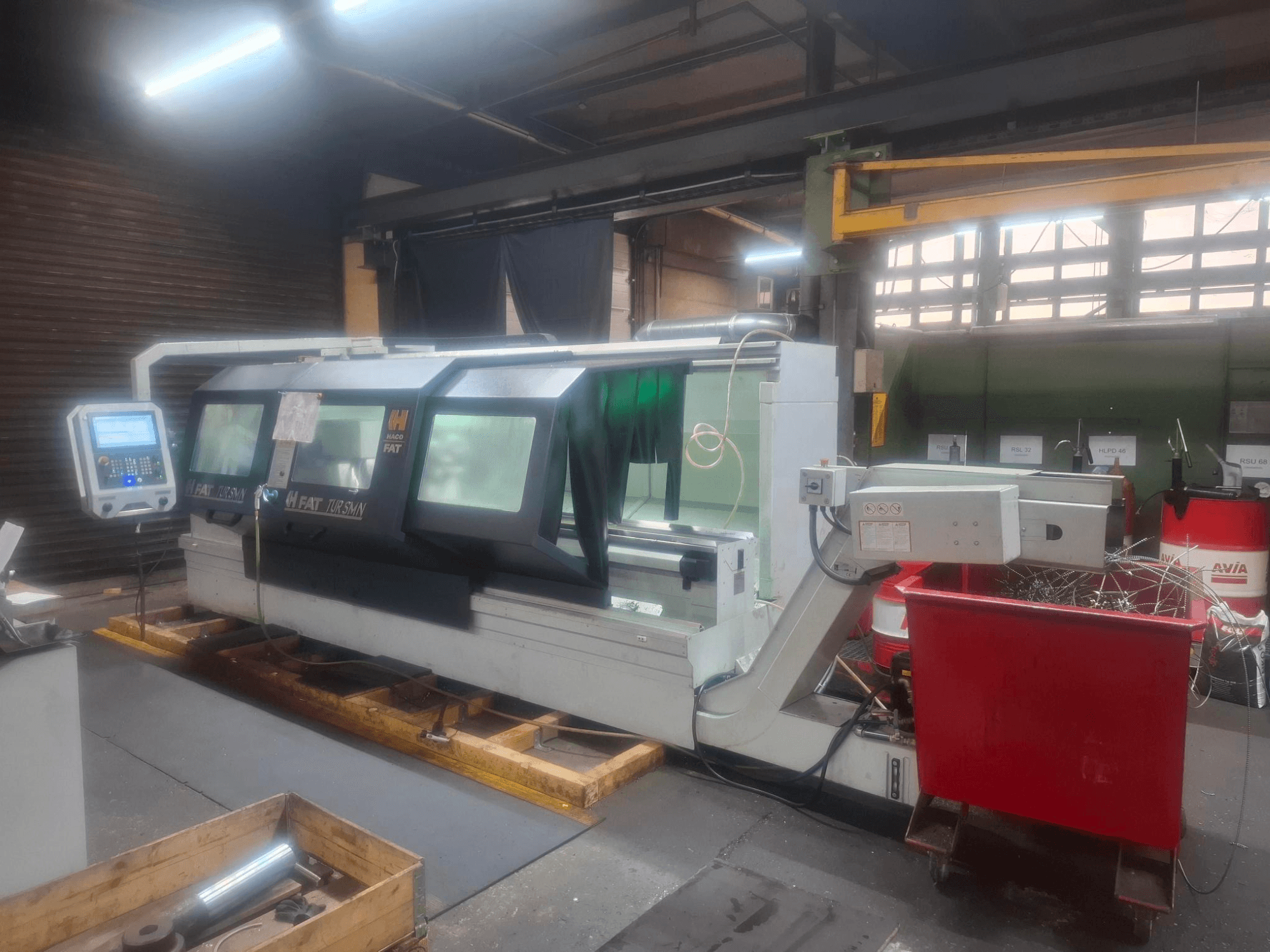 Vue de face d'une machine CNC FAT Tursan avec panneau de commande, placée sur des palettes en bois dans un atelier.