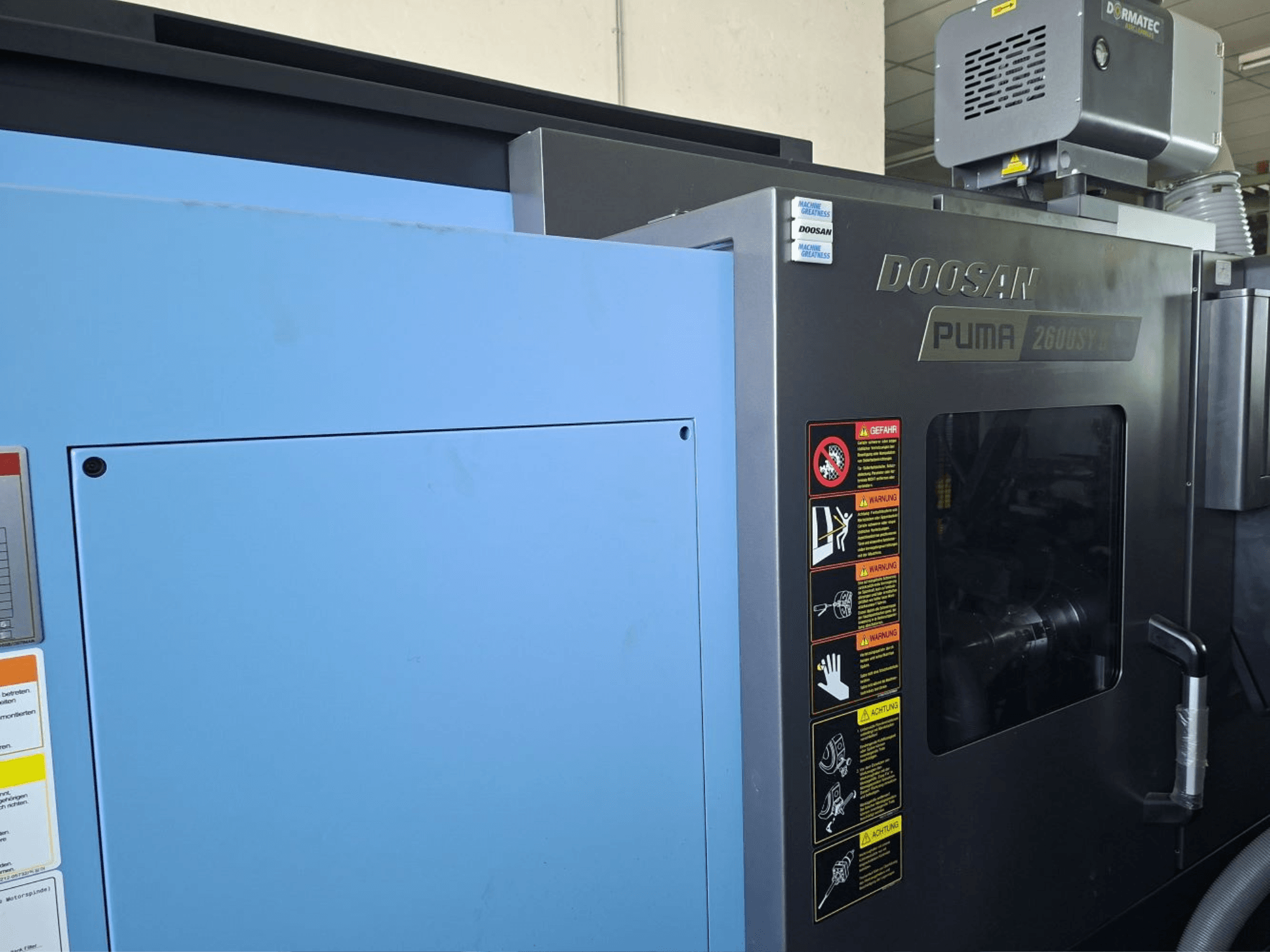 Tour horizontal DOOSAN PUMA 2600 SY II, vue de face, présentant les étiquettes de sécurité et les panneaux bleus.