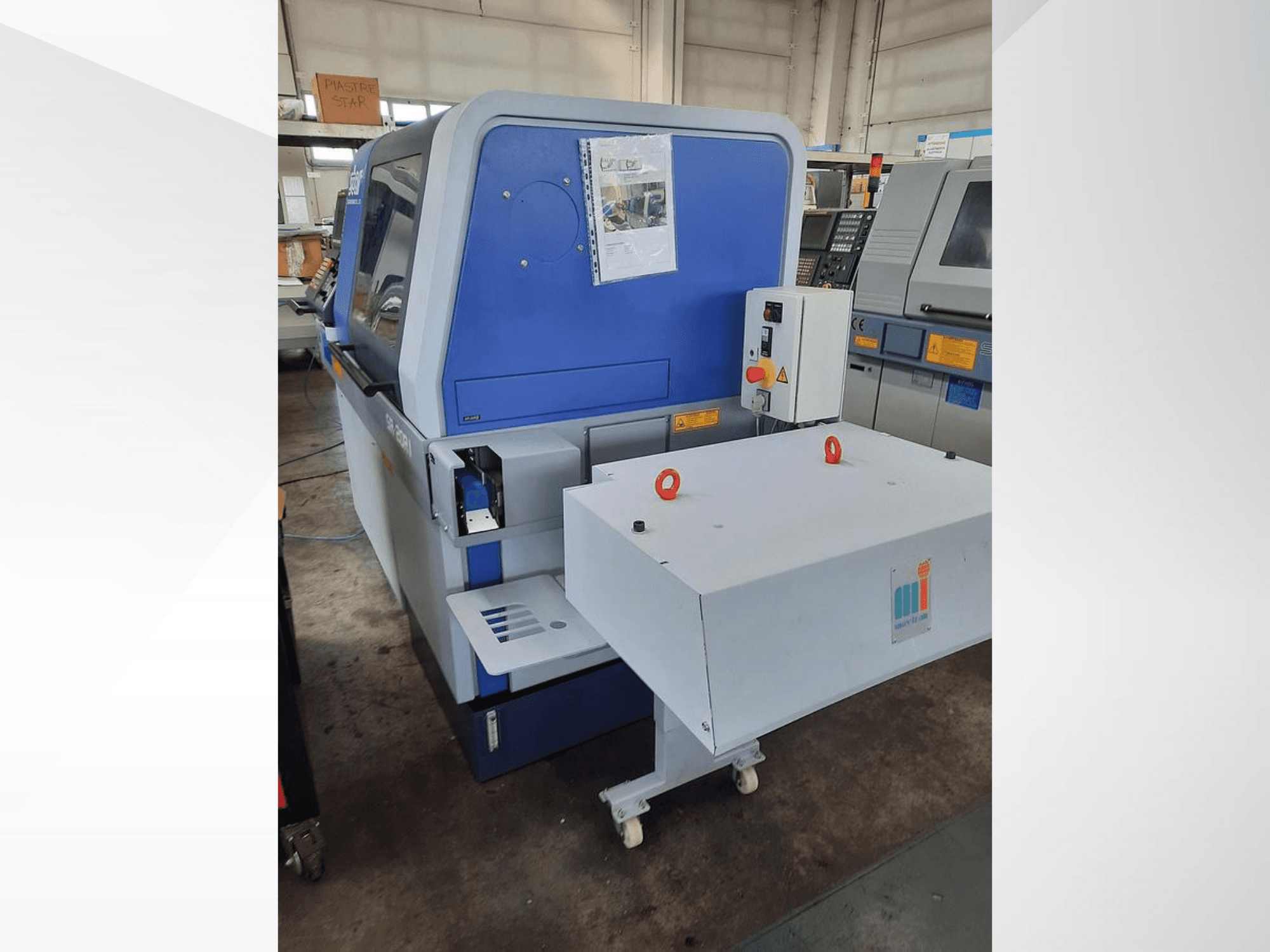 Machine industrielle bleue avec un convoyeur blanc, montrant le panneau de commande et les dispositifs de sécurité attachés, vue de côté.