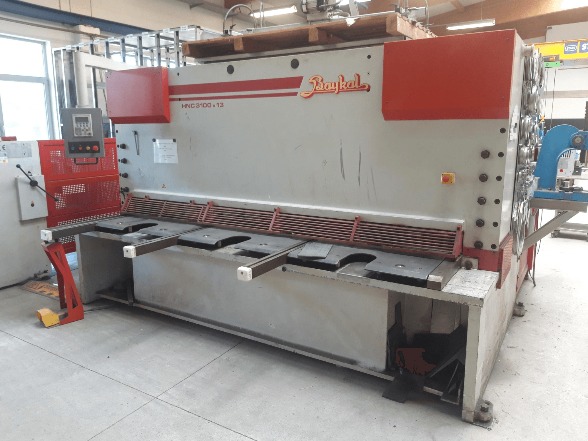 Vue de face de la cisaille CNC Baykal HNC 3100x13, avec son panneau de commande, sa zone de découpe des métaux et son espace de collecte des déchets.