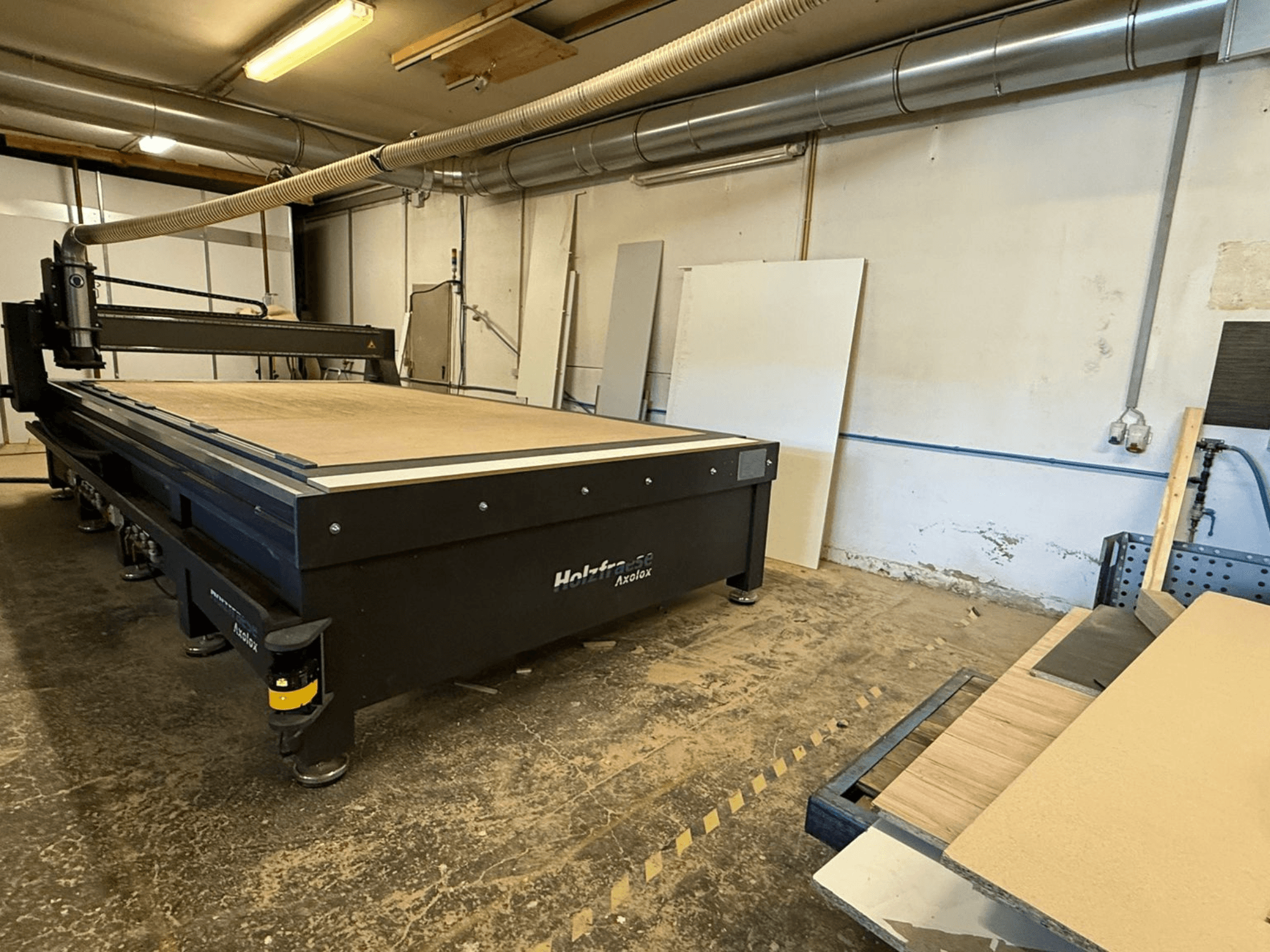 Défonceuse CNC Holz-Her Axos 5 dans l'atelier, vue de face montrant la table de travail, le système d'extraction des poussières et les panneaux de bois à proximité.