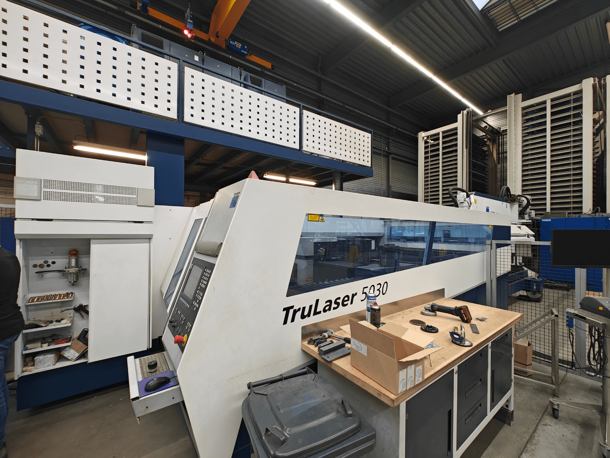 Machine TruLaser 5030 dans un atelier, vue de face avec panneau de commande visible, entourée d'outils et d'équipements.