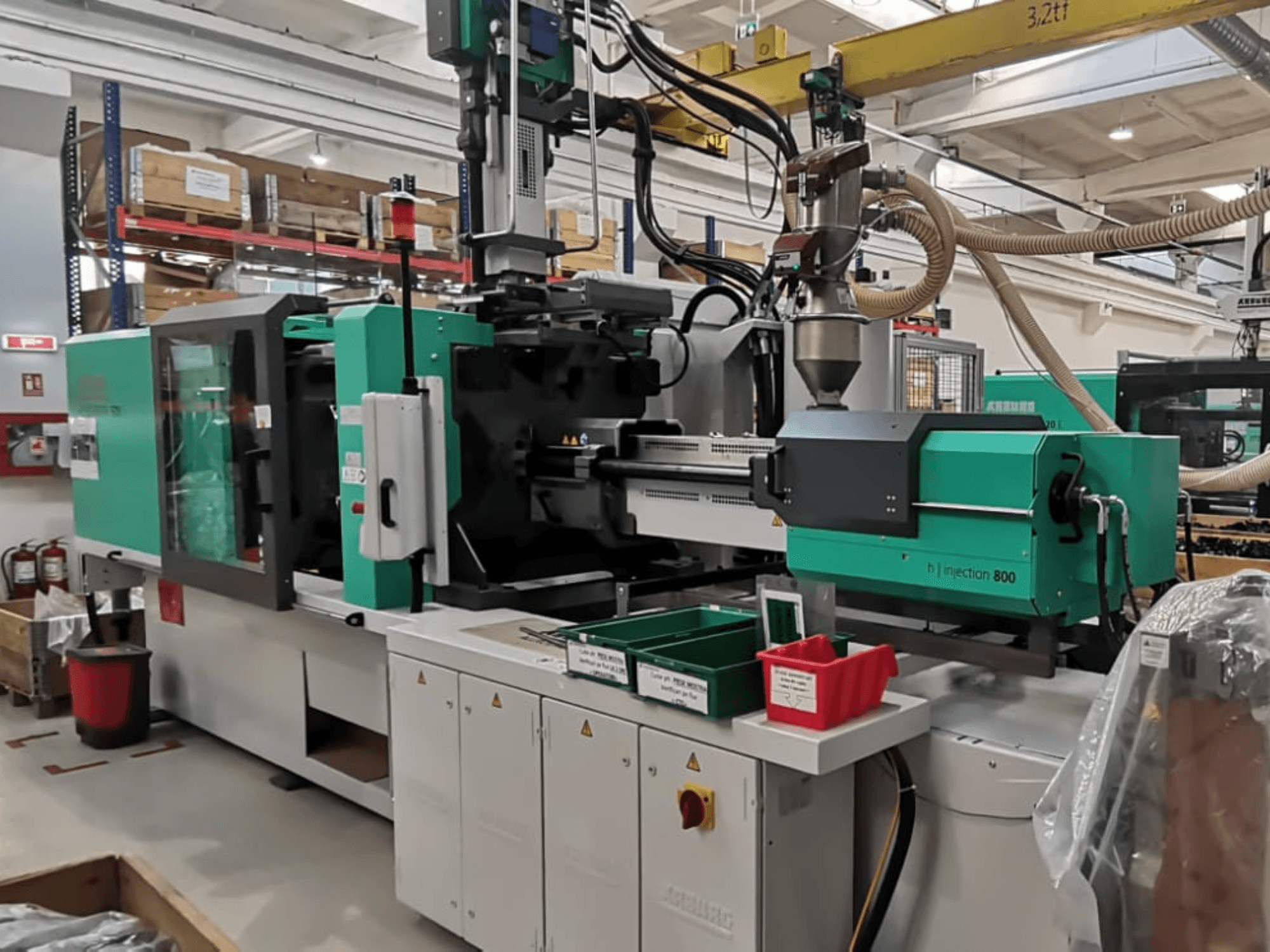 Machine d'injection 800 en H dans une usine, vue de face, avec un design vert et noir, des panneaux de commande et des bacs pour les pièces.