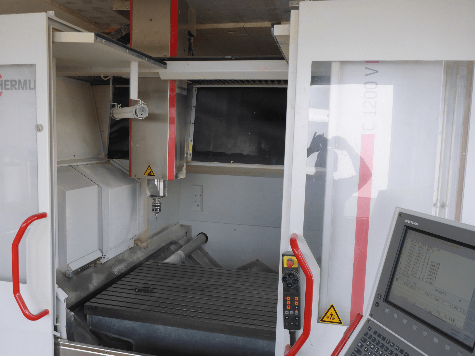 Intérieur du centre d'usinage vertical HERMLE C 1200 montrant le porte-outil, le panneau de commande et la table de travail vus de face.