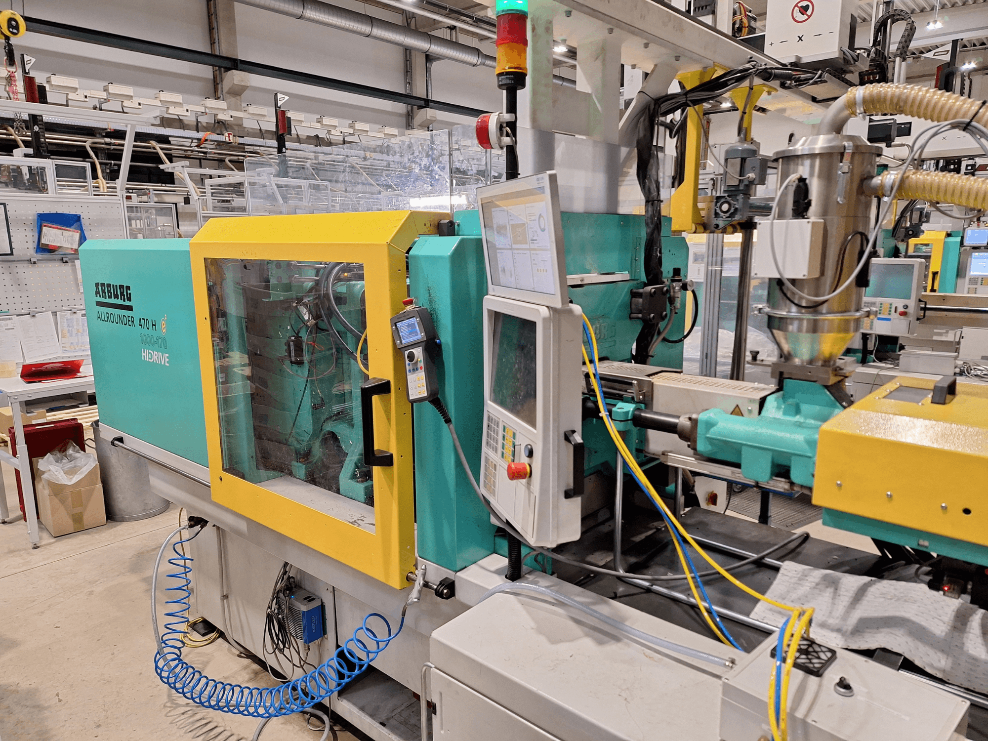 Machine de moulage par injection hydraulique Arburg 470 H 1000-170, vue latérale montrant le panneau de commande et le système d'alimentation.