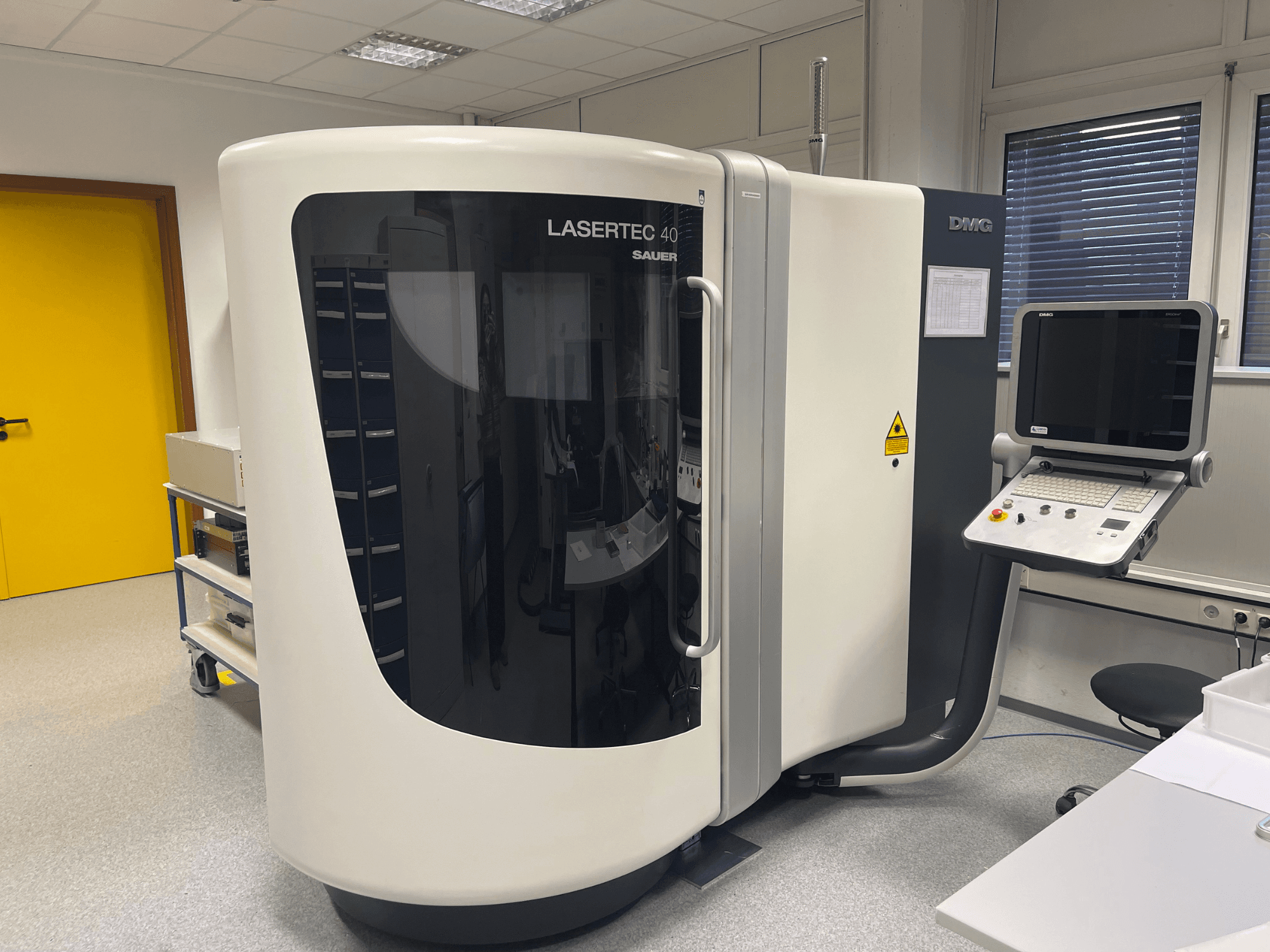 Fraiseuse LASERTEC 40 blanche de DMG MORI, vue de face, panneau de commande et conception ergonomique dans une salle bien éclairée.