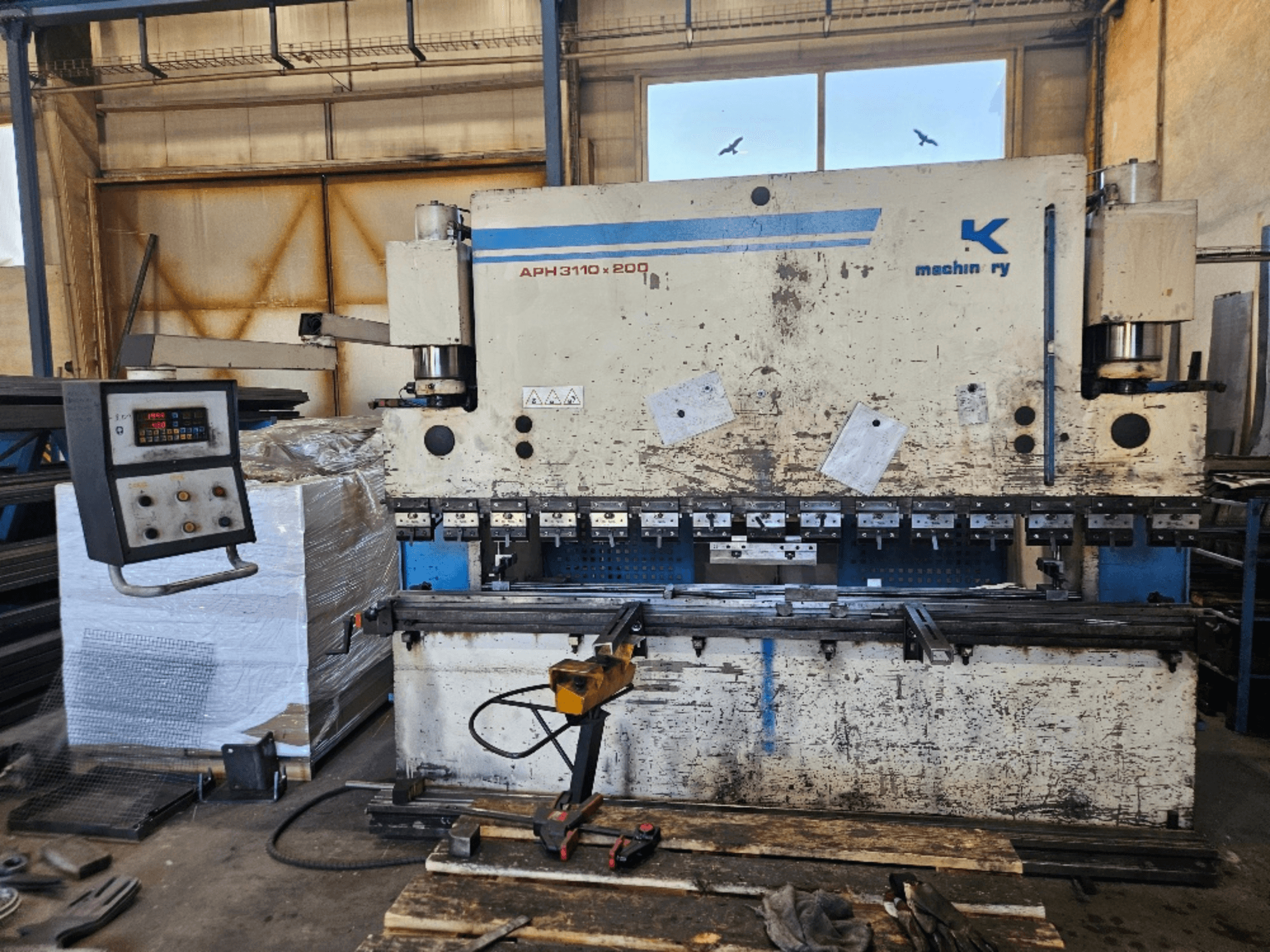 Presse plieuse Baykal APH 3110x200 dans un atelier, vue de face, avec panneau de commande, tôles et outils visibles.