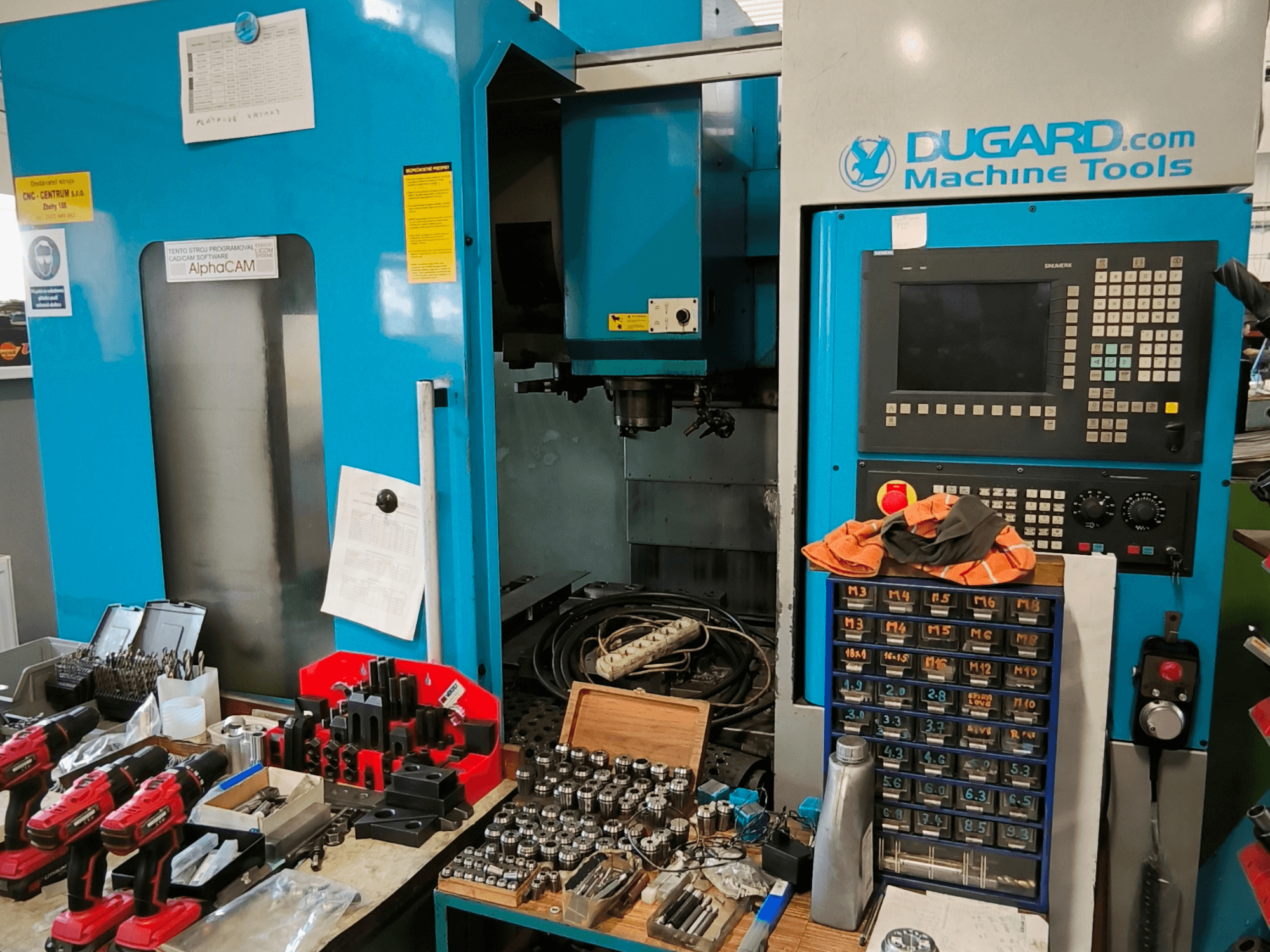 Vue de face du centre d'usinage vertical Dugard 850VMC, présentant le panneau de commande, les outils et les accessoires sur un établi.