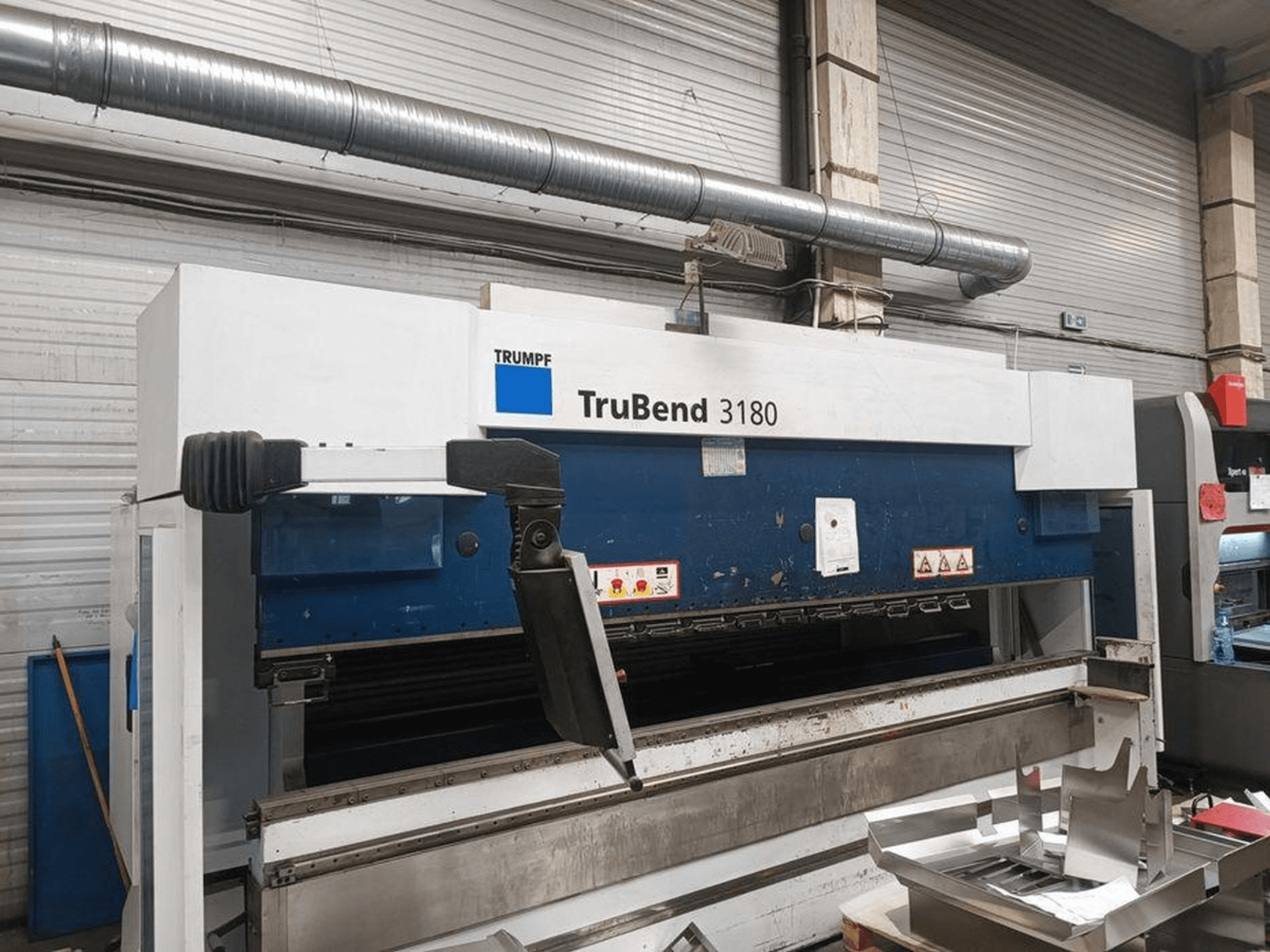 Machine à cintrer Trumpf TruBend 3180 dans un atelier, vue latérale montrant le panneau de commande et les pièces métalliques sur la table.