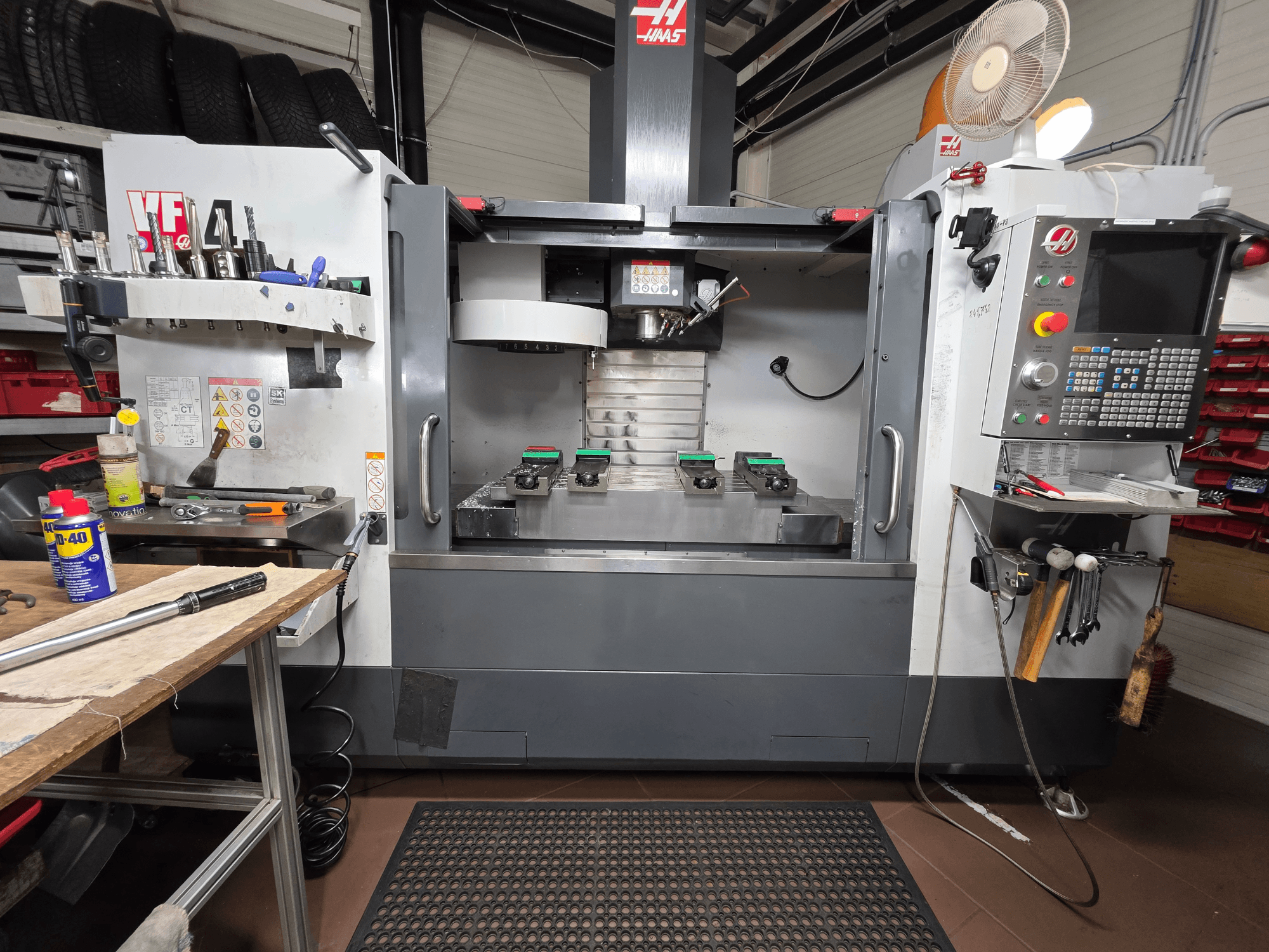 Vue de face de la fraiseuse CNC Haas VF-4 dans un atelier, avec des outils, une interface informatique et deux pièces à usiner sur la table.